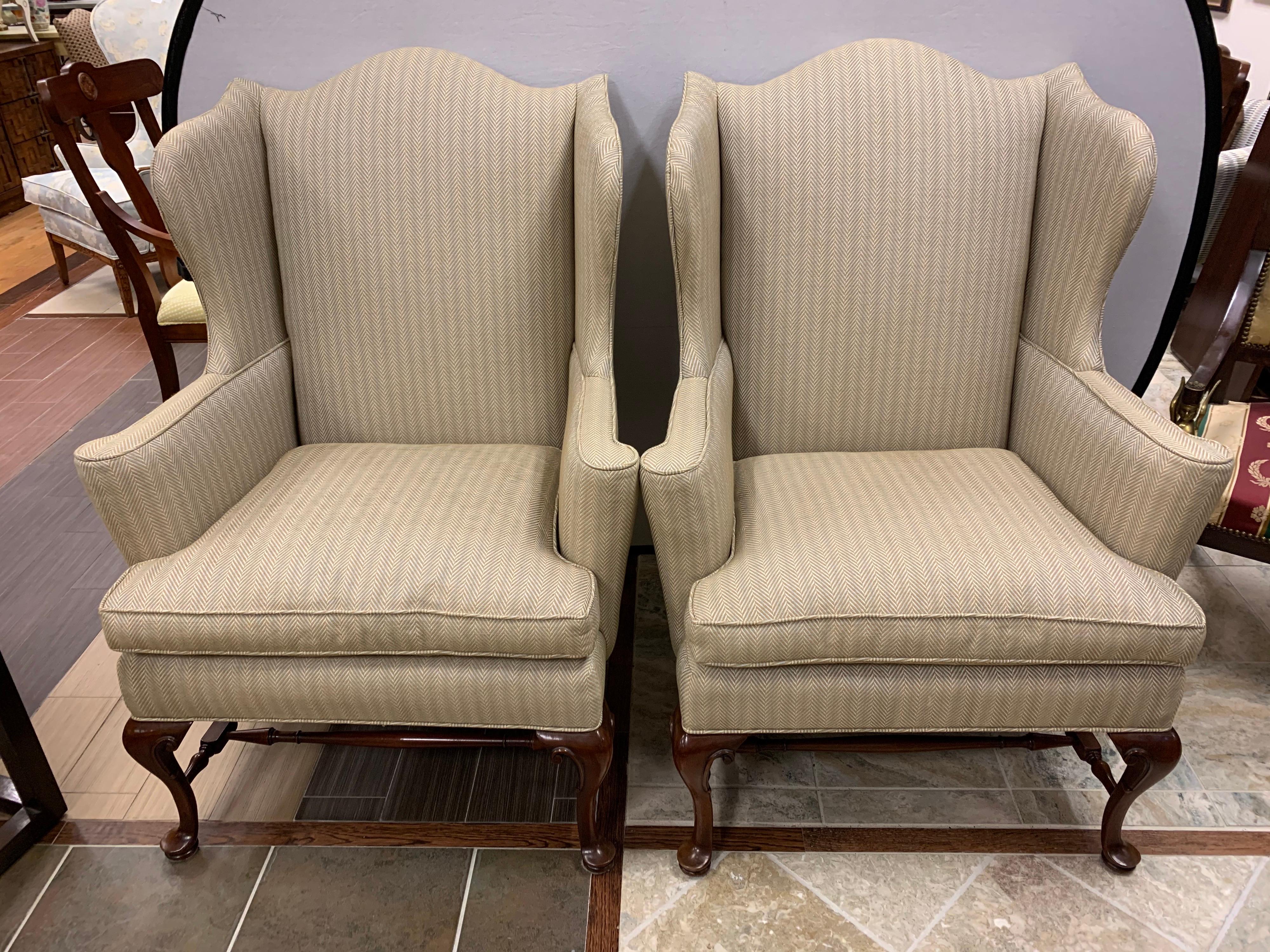 Pair of matching Henredon Furniture wingback chairs with newer upholstery. Fabric is a cotton blend in an olive, gray and blue weave (see attached photos). They sit on a mahogany frame supported by cross stretchers. 