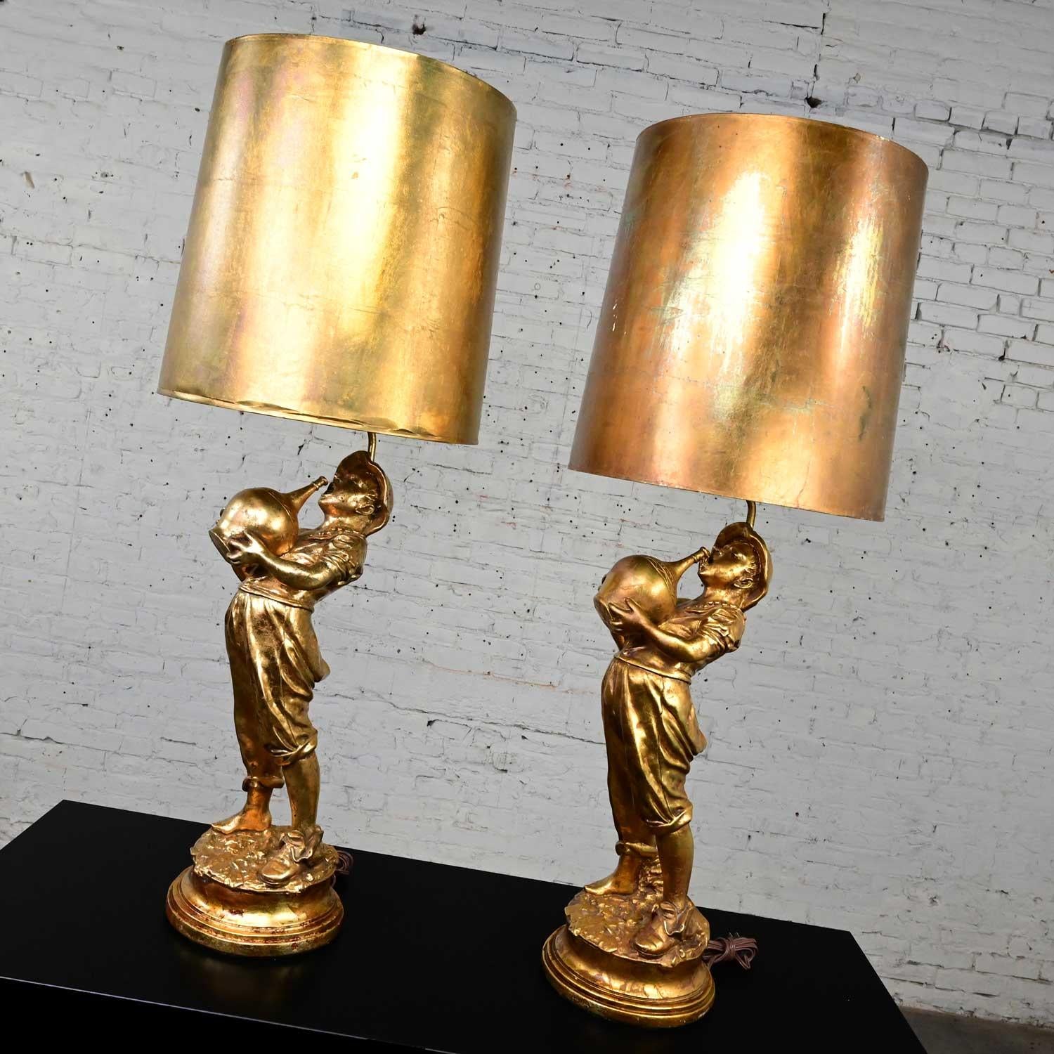 Fabulous pair of midcentury Hollywood Regency hand gilded gold plaster large scale figural lamps boy with drinking jug and original slightly tapered gold leafed or gilded drum shades in the style of Marbro Lamp Company. Beautiful condition, keeping