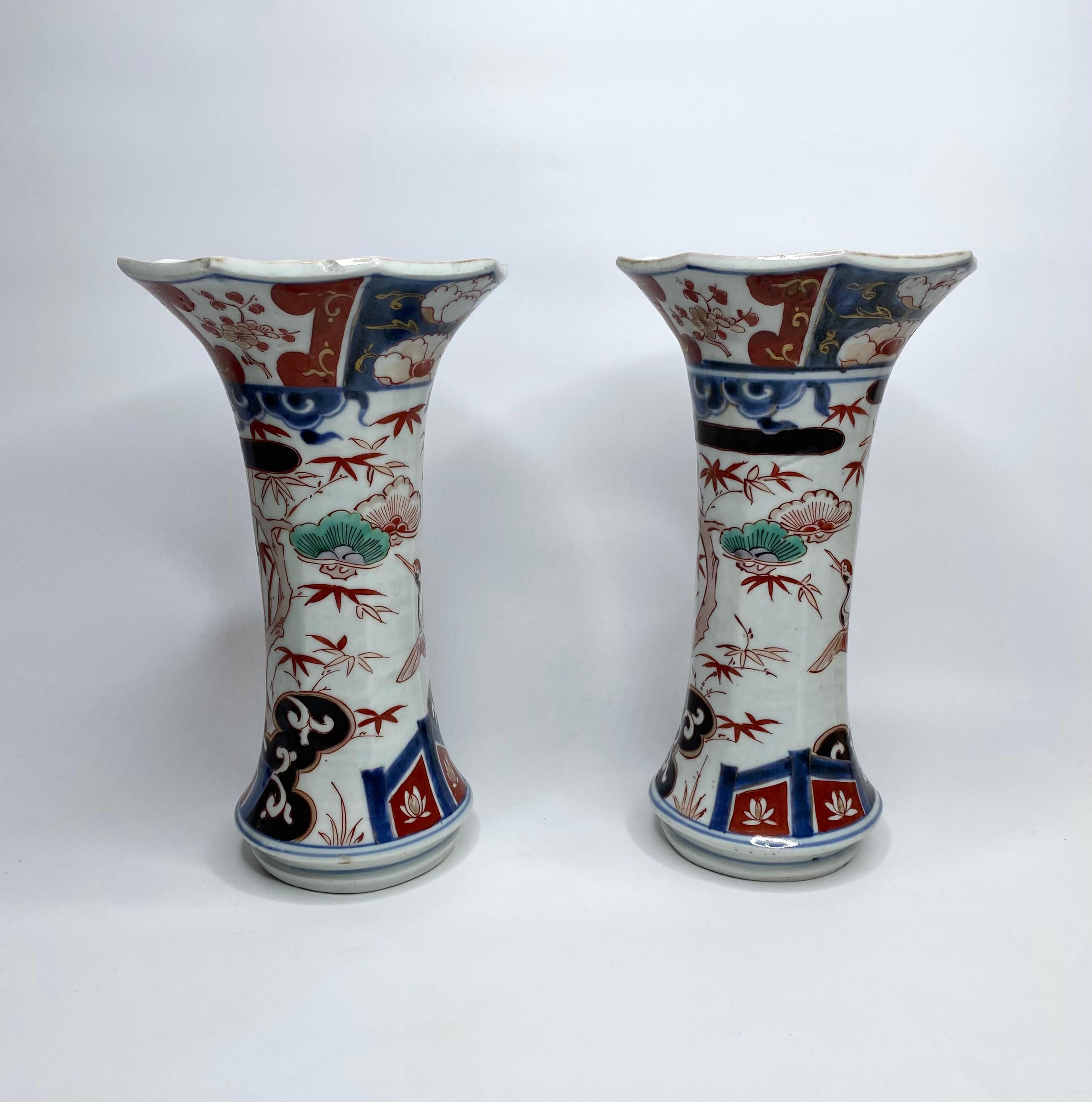 Pair of Japanese porcelain ‘Imari’ vases, Arita, c. 1700, Genryoku Period. The hexagonal shaped vases, hand painted in the Imari style, with storks flying amongst flowering prunus trees and bamboo plants, beneath clouds. The rim, painted with panels