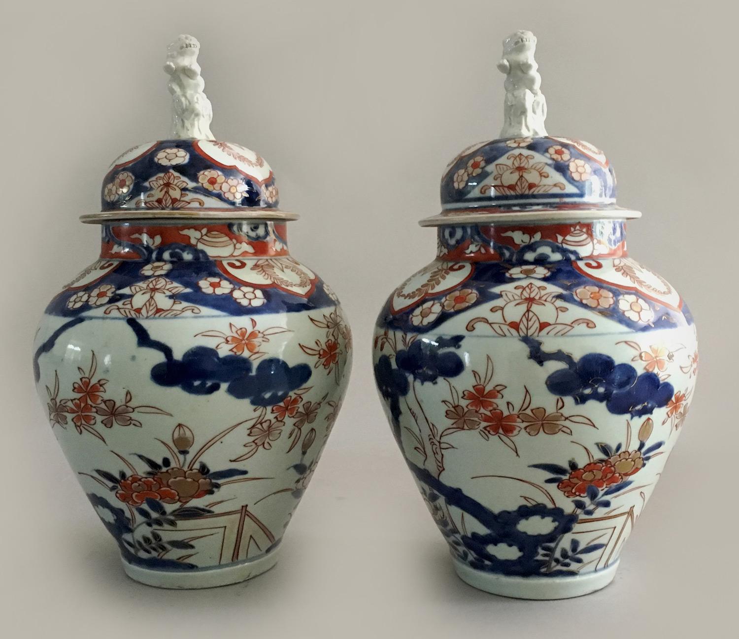 Antique pair of Imari vases and covers with foo dog finials, the body decorated with cobalt blue branches and floral designs, the shoulders with half-shield shapes outlined in orange and floral patterns.