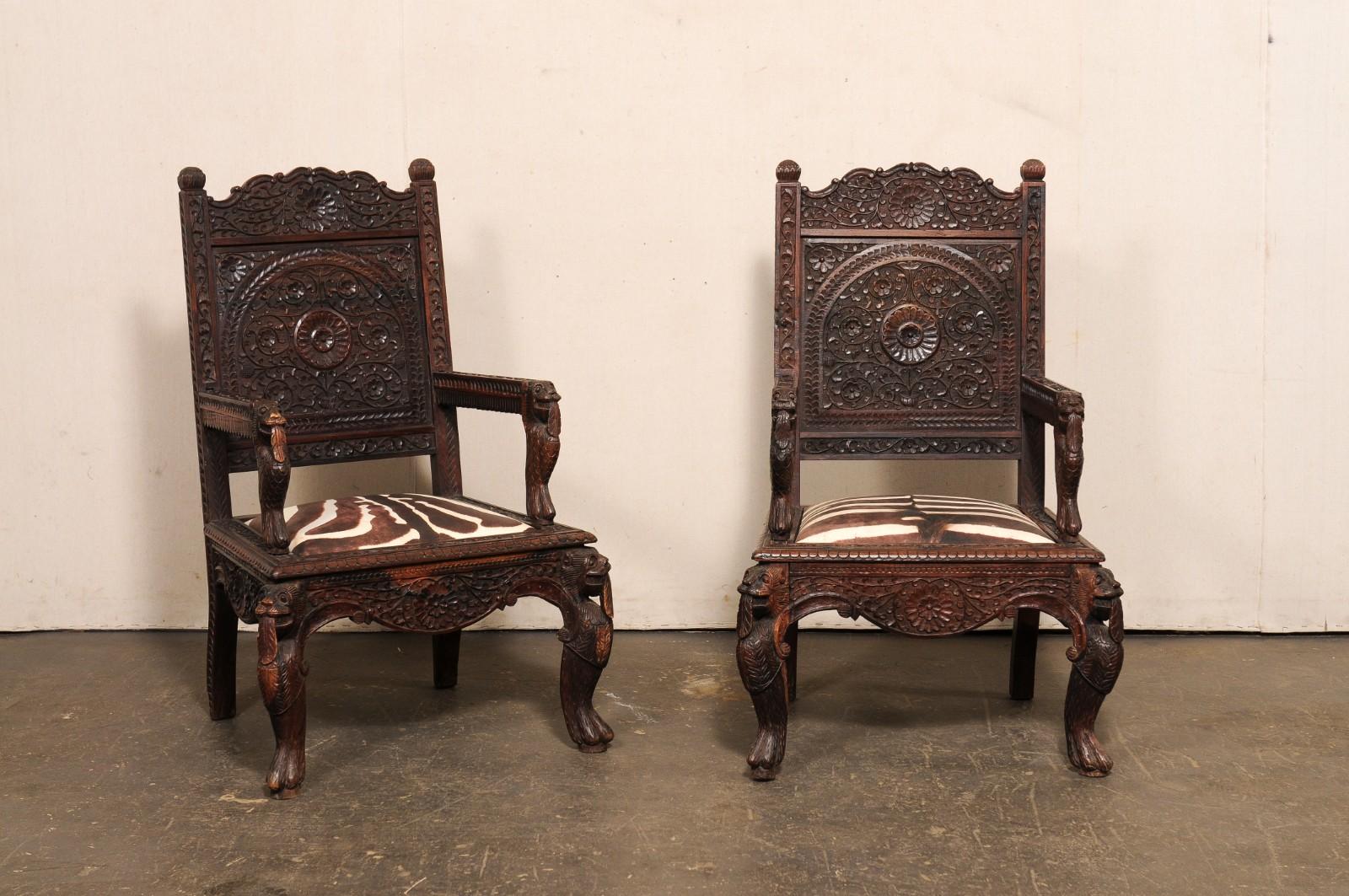 Paire de fauteuils indiens richement sculptés, à l'assise zébrée, du milieu du 20e siècle. Cette paire de fauteuils vintage de l'Inde présente des sculptures élaborées de motifs floraux, de figures mythologiques et de motifs géométriques sur