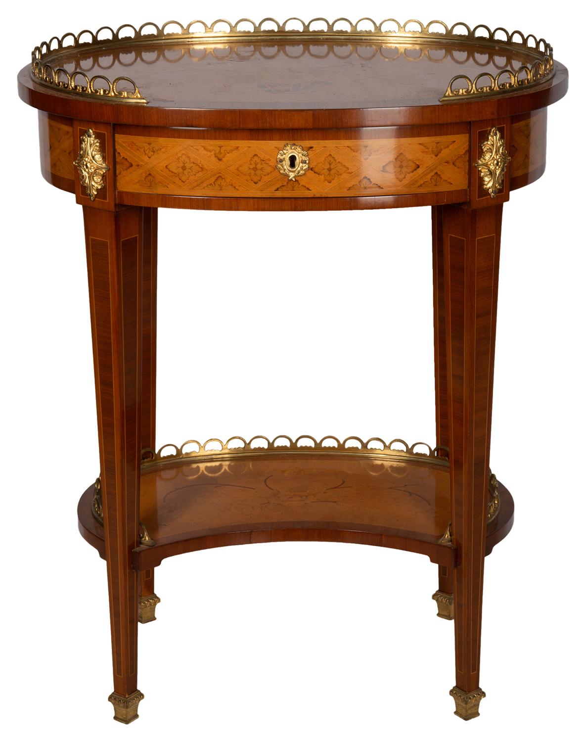 A pair of French oval inlaid Louis XVI style side tables, each with an ormolu three quarter gallery to the tops, inlaid floral decoration the top and under tier. Having single frieze drawers also with inlaid, raised on square tapering legs and