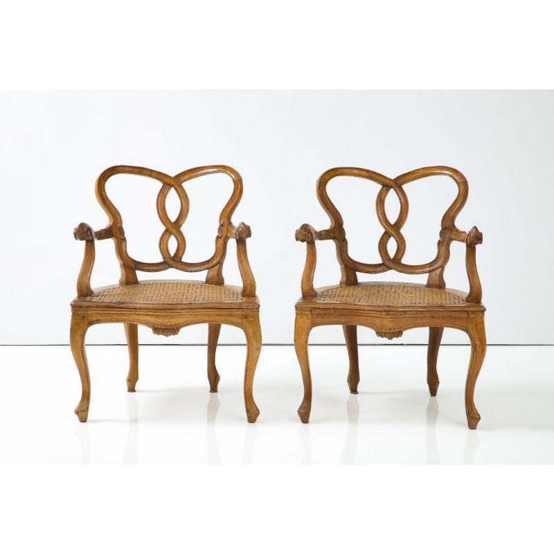 A pair of oak Italian side chairs with carved back and arms and cane seating. Original finish and cane and a custom cushion would complete the look. Minor wear in the cane. Measure: 15