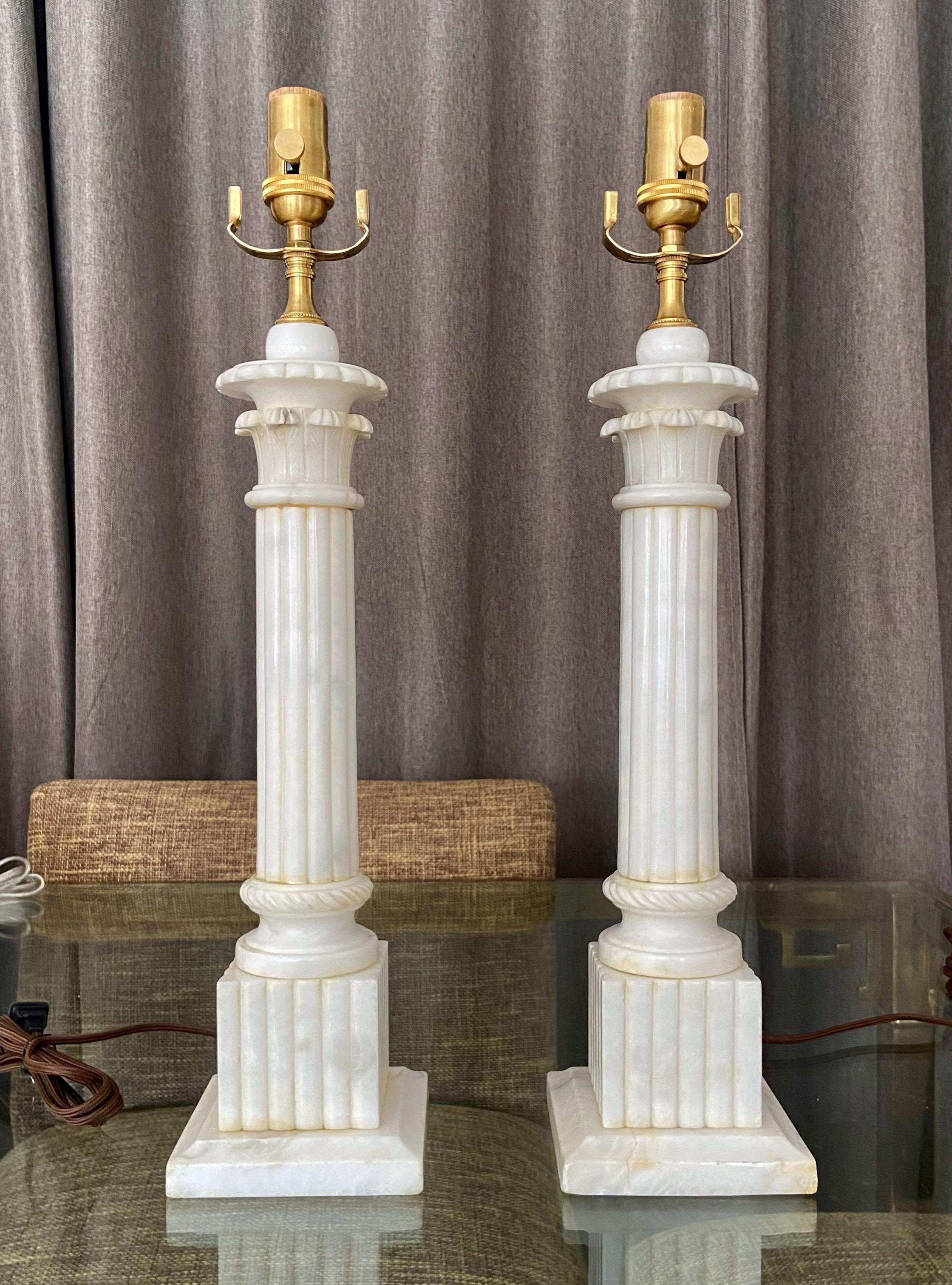 Pair of neoclassical style carved column form alabaster table lamps. Newly wired with new brass 3 way sockets and rayon cords. 
Measures: height to top of alabaster is 18