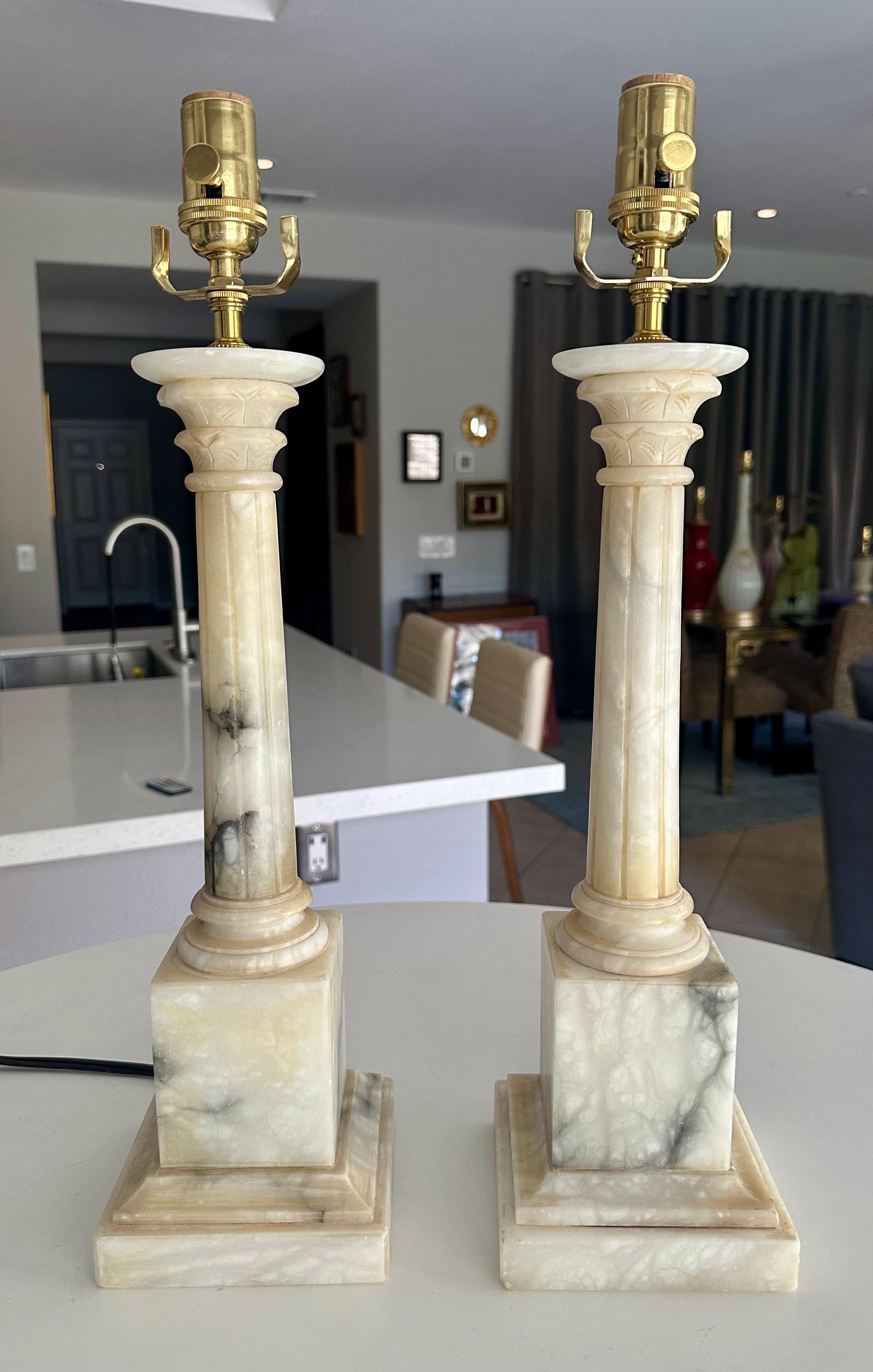 Pair of neoclassical style carved column form alabaster table lamps. Lots of nice natural viewing throughout. Newly wired with new brass 3 way sockets and cords. 
Measures: height to top of alabaster is 16
