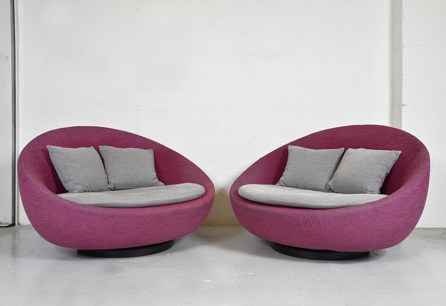 Pair comfy Lacoon swivel love seats designed by Jai Jalan and made by Désirée, Italy. Each couch has a metal and solid wood oval frame which swivels effortlessly on a circular metal base. 
Both couches have the original two-tone loose covers in a
