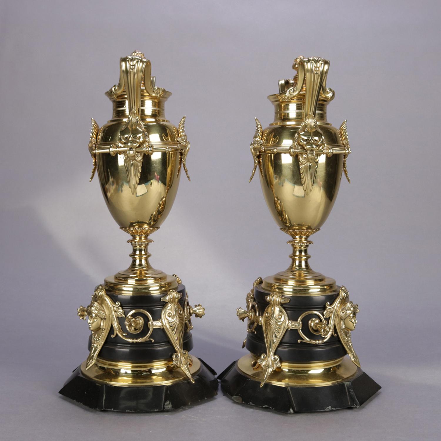 Pair of Italian figural Egyptian Revival urns feature polished bronze double handle urns having scroll form handles with masks and seated on stepped marble bases with scroll and foliate decoration with Cleopatra masks, cord receiver for lamp
