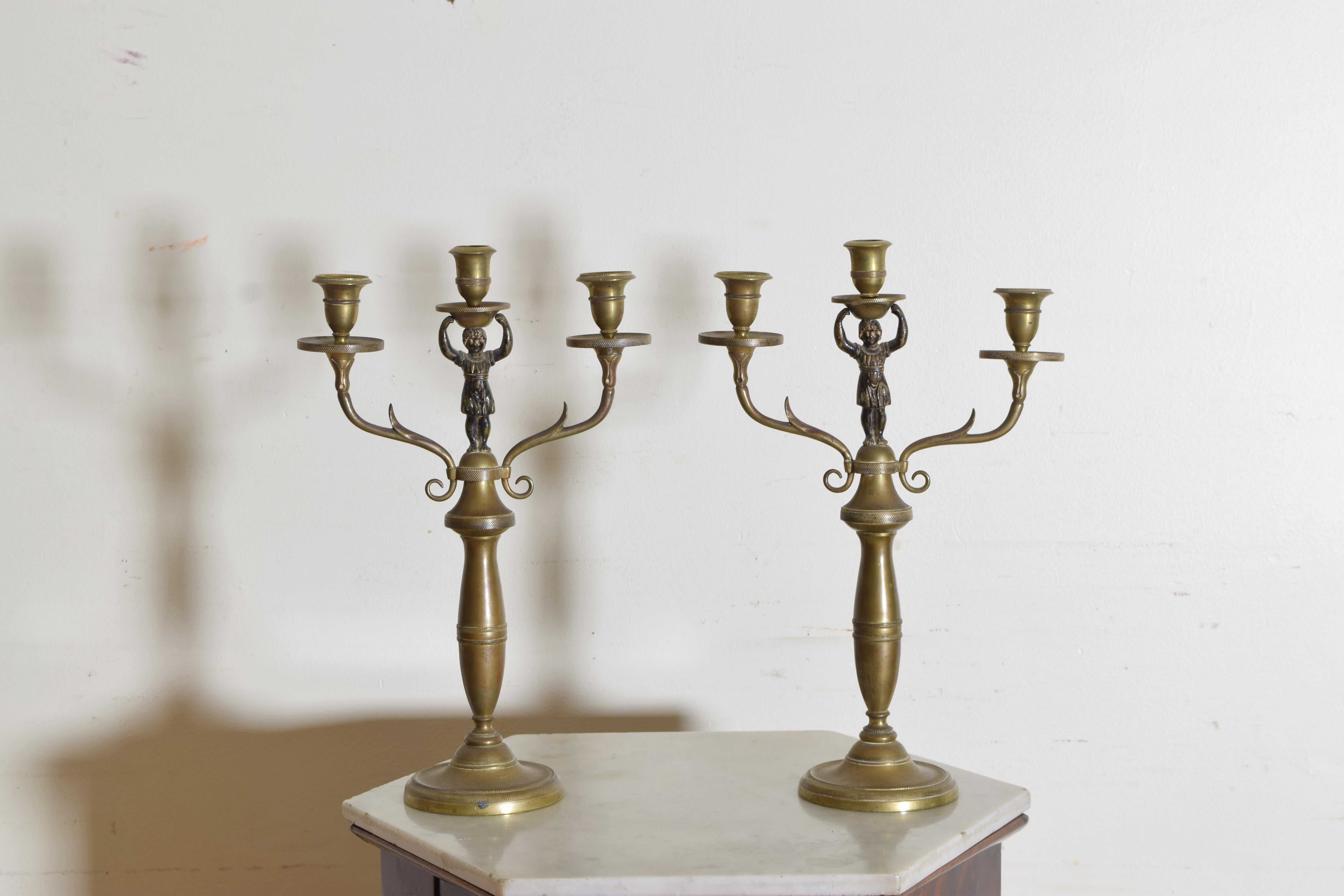 Finely cast and supported by circular bases, the tops issuing two arms with single candleholders with a central figural candleholder.