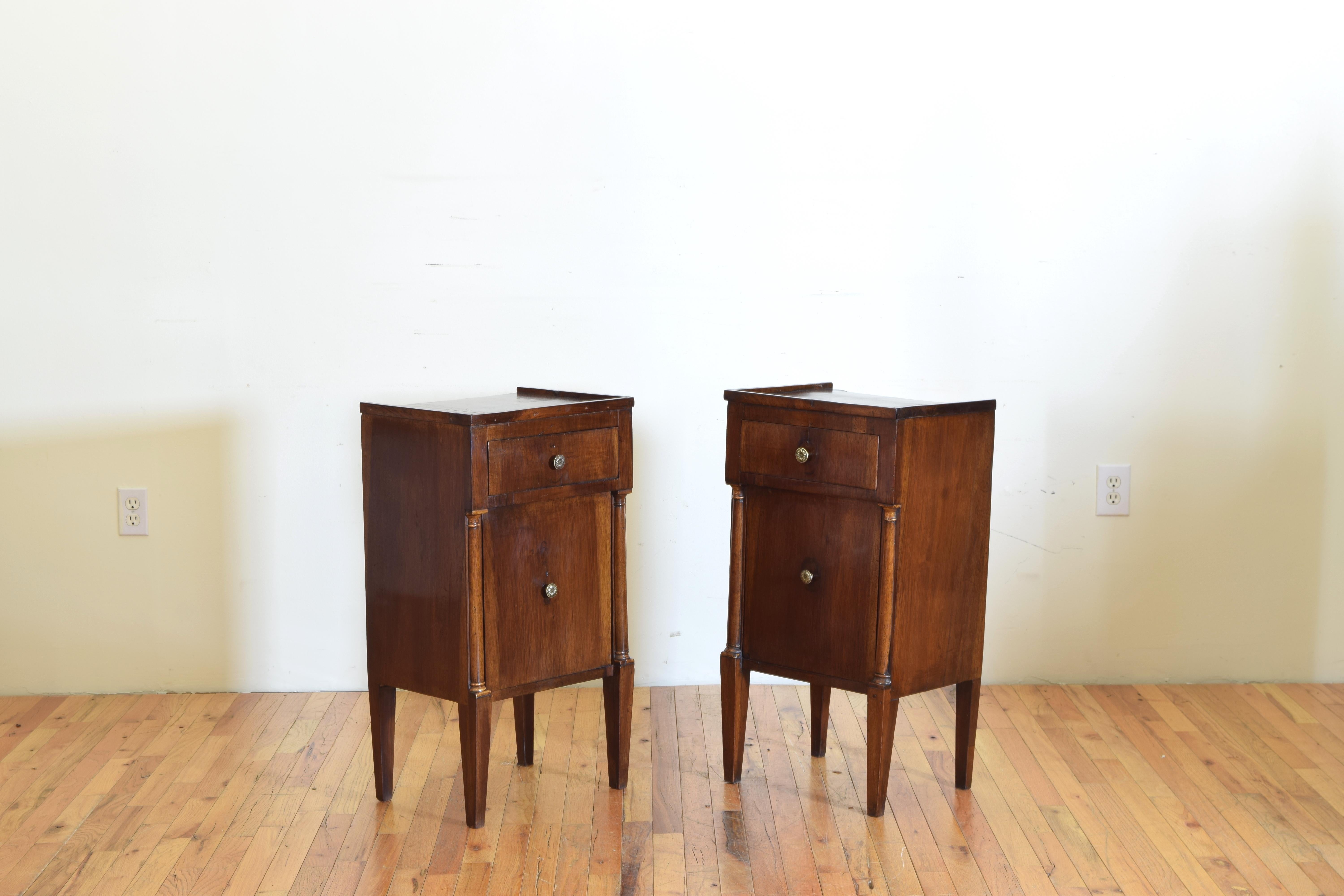 Having galleried tops with one drawer over one door, the doors flanked by half columns and faded giltwood capitals, with brass hardware, raised on square tapering legs, first of the 19th century.