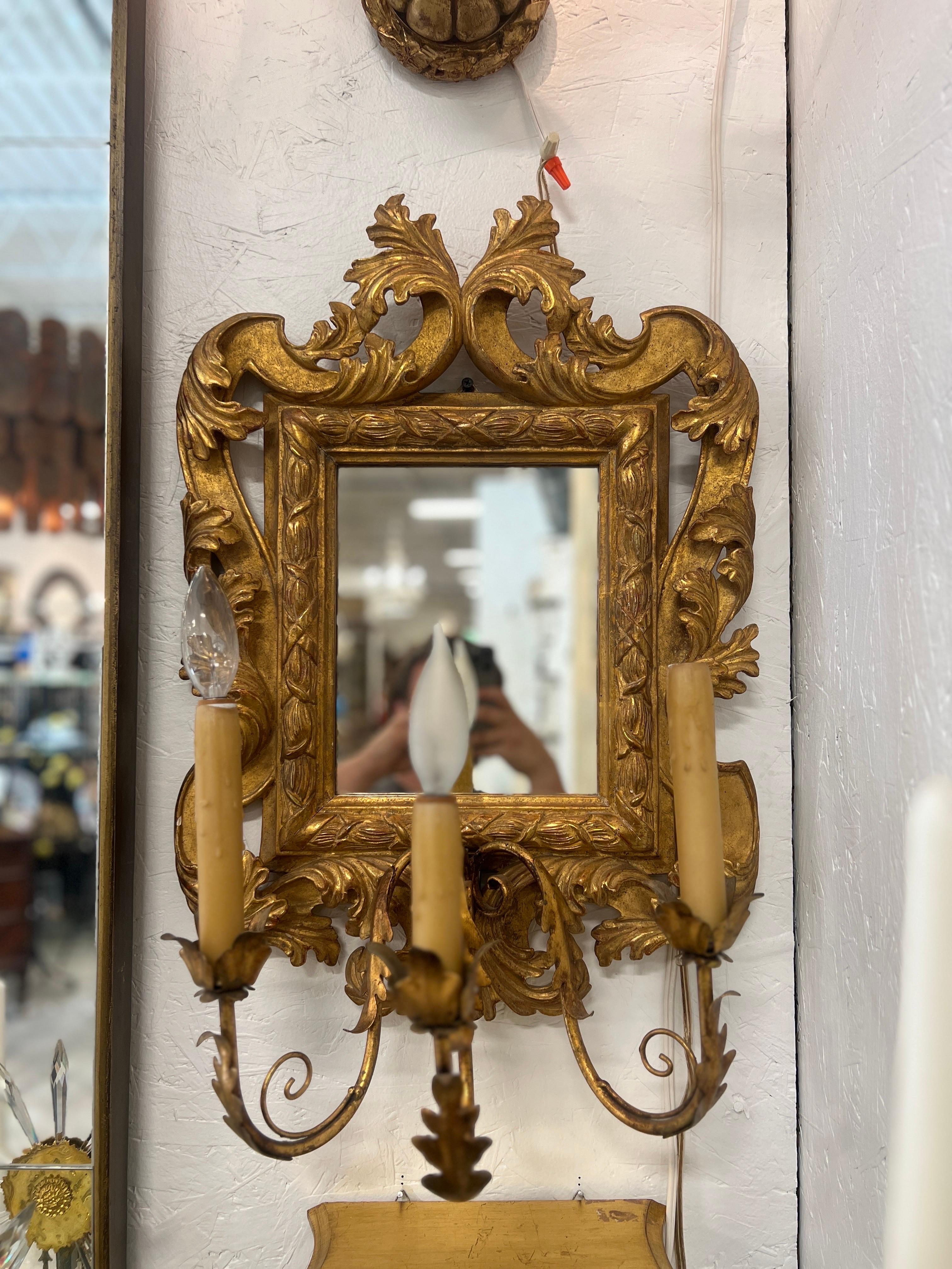 Italian, 20th century.

A pair of vintage Italian made giltwood mirrors with a fine Rococo style frame, acanthus leaf carvings and three tole acanthus arms. Each arm is electrified with wax candle covers and in working condition. Marked to verso