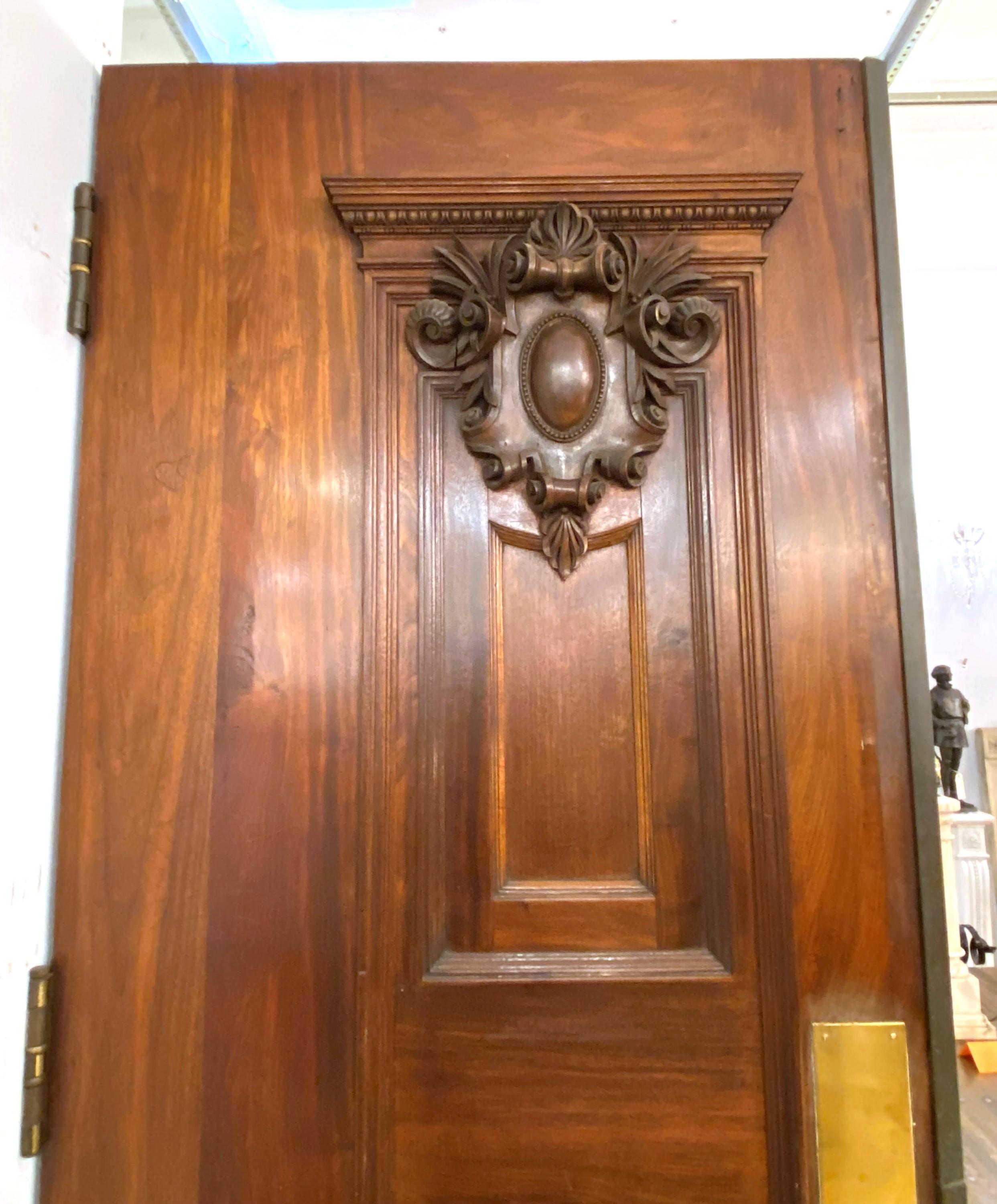 Early 20th century pair of extra thick solid walnut doors. Each door features a hand carved cartouche in front. One lower panel was replaced with glass. Priced as a pair. Please note, this item is located in one of our NYC locations.
