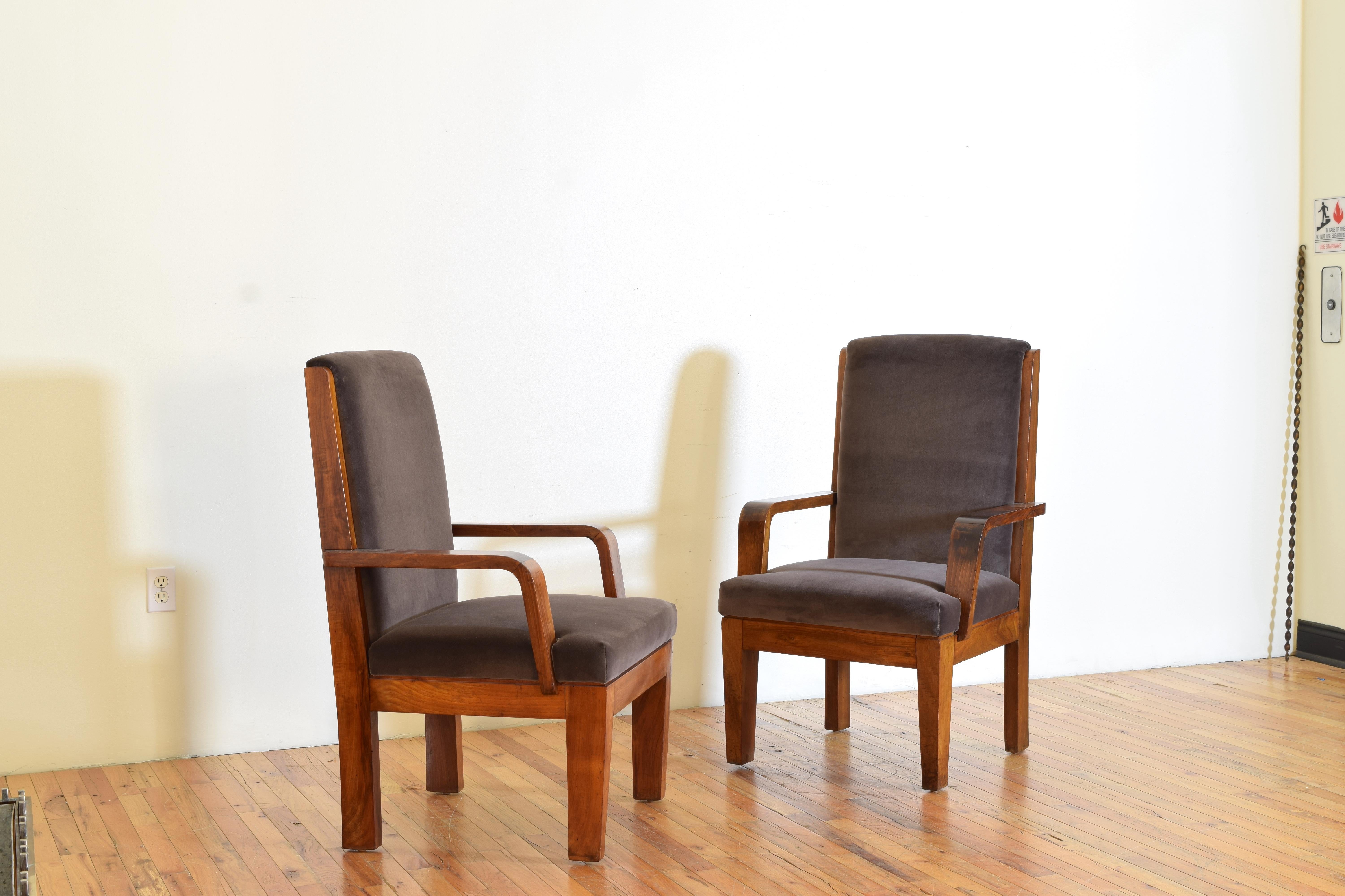Each chair with a slightly arched backrest the upholstered back within a walnut framework that continues to the rear of the chair, the padded inset seat below rounded armrests, the legs are block and slightly tapering