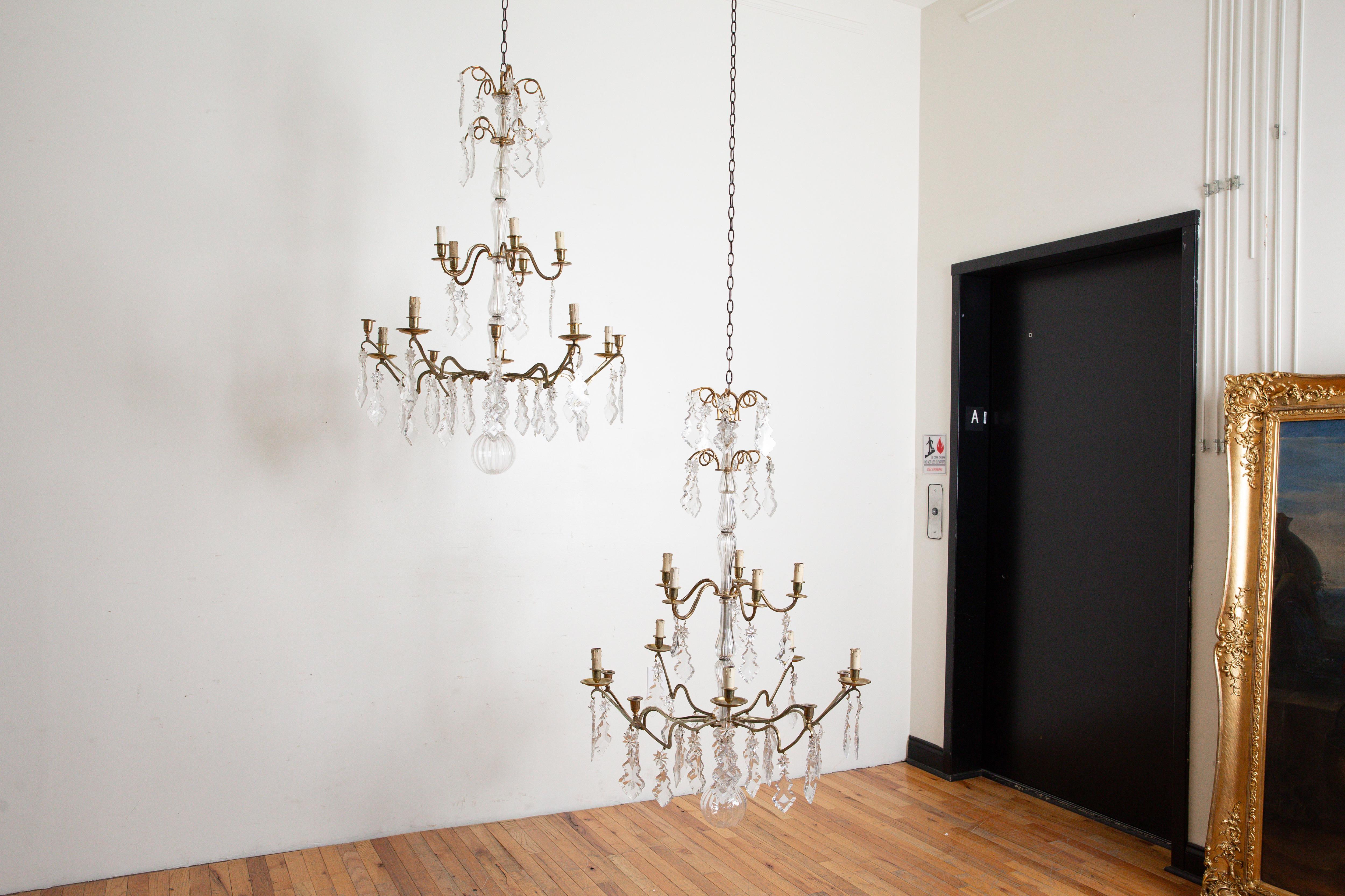 each chandelier with shaped and segmented glass standards issuing two upper levels of curled bronze arms with hanging prisms, the two lower levels each with candle cups and bobeches, made for candlelight these fixtures will be outwired for