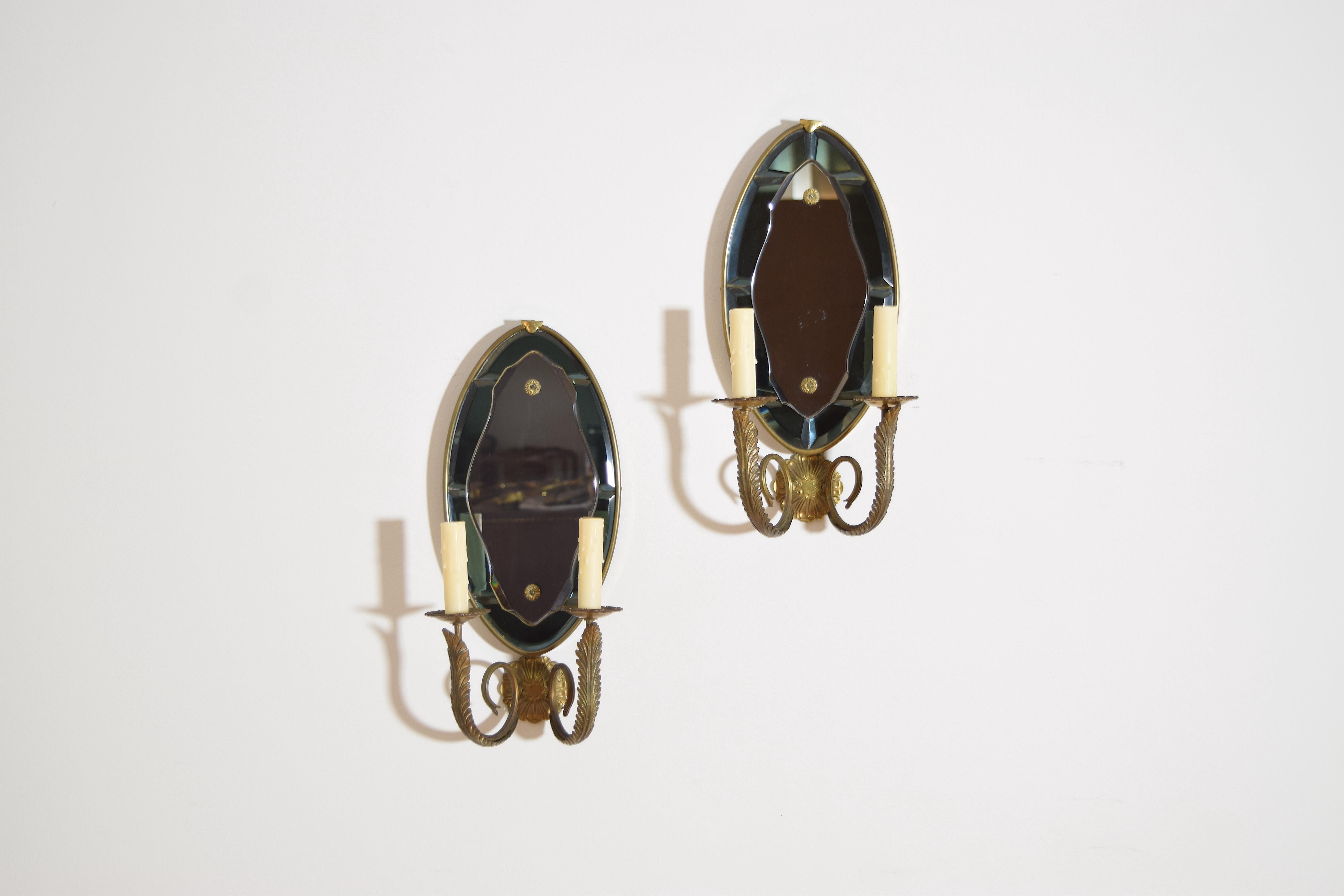 of oval form with faceted glass and beveled surfaces, the backplates issuing two brass arms, wired