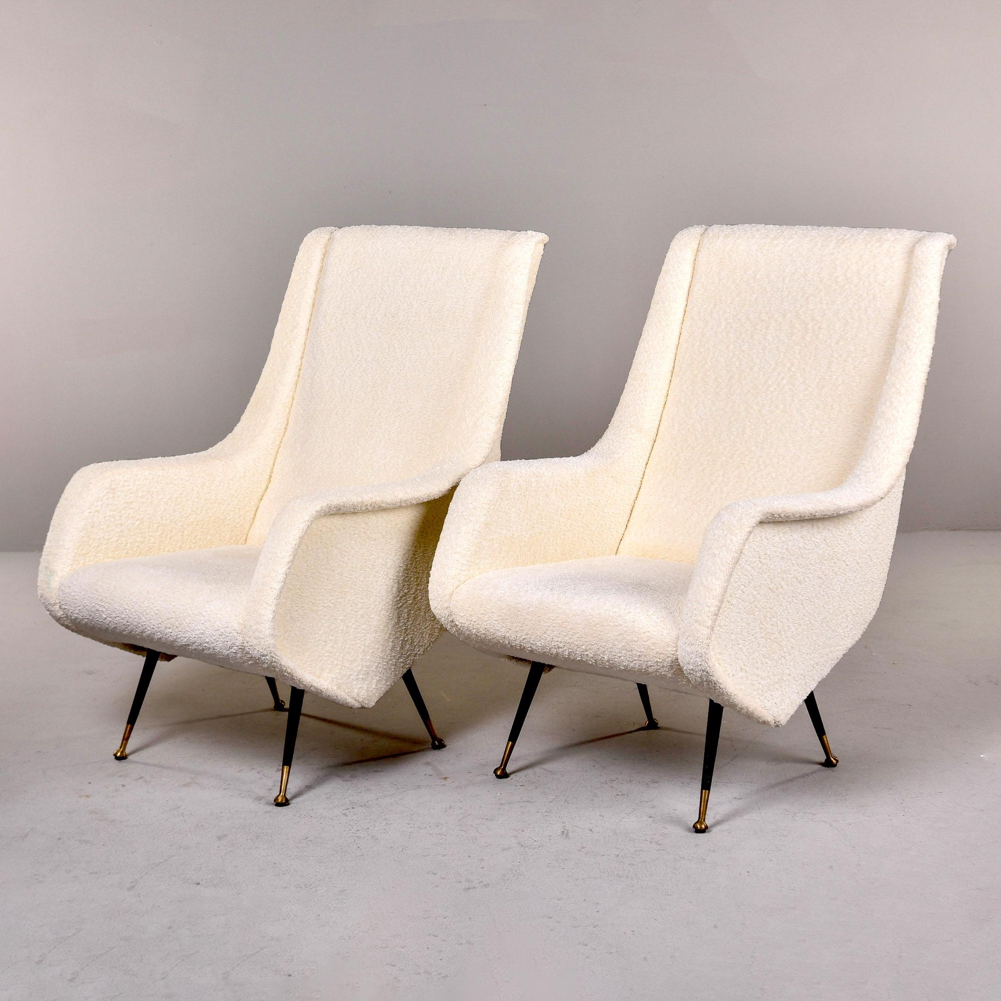 Found in Italy, this pair of lounge chairs dates from the 1950s. Fun, sculptural lines with high back rests, curvy sides and slender black metal legs with brass feet, these chairs have a distinct vintage Italian flair. Newly upholstered in a creamy