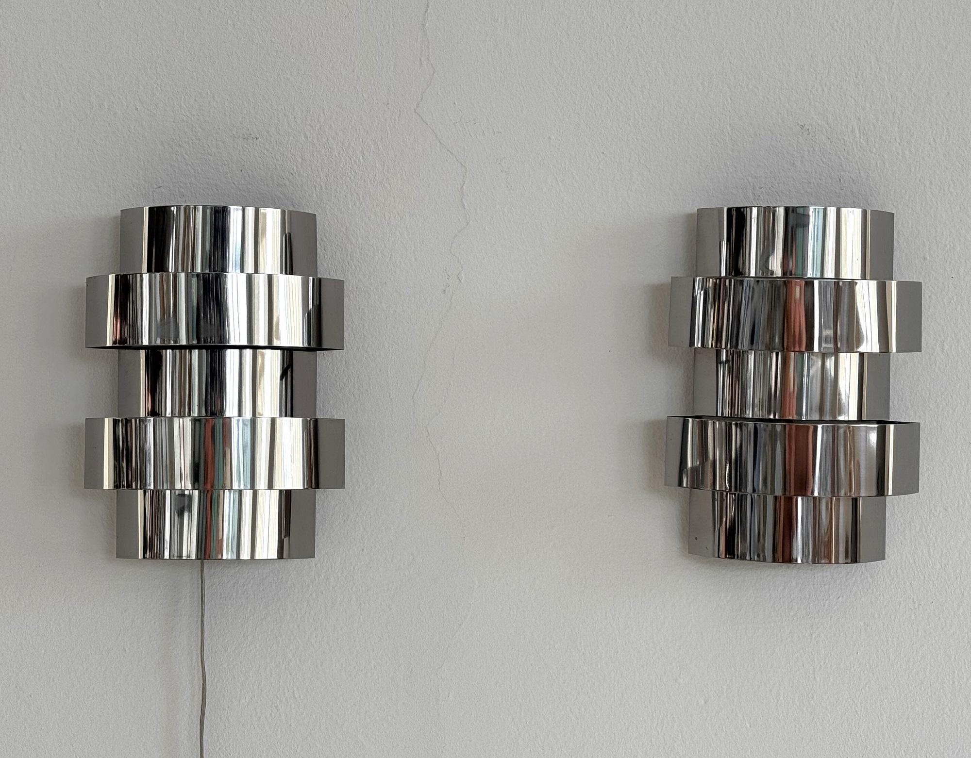 Paar italienische Chrom-Wandleuchten aus der Mitte des Jahrhunderts von Goffredo Reggiani, 1970er Jahre

Minimalistisches, modernes und glänzendes Paar Wandleuchten aus rostfreiem Stahl.
Die Montageplatte besteht aus lackiertem Metall.
Die