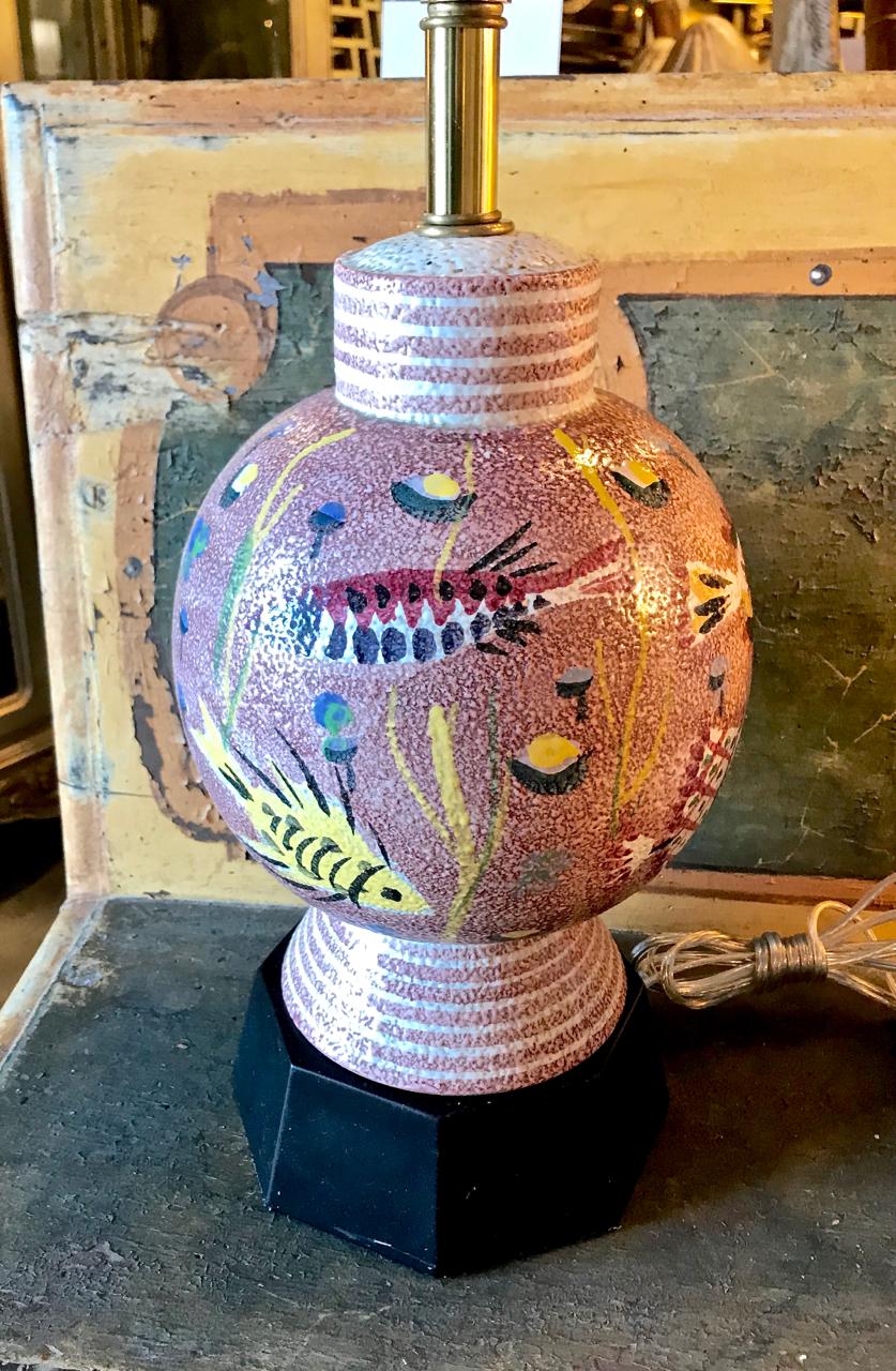 This is a fun pair of Italian pink pottery lamps that have been attributed to Fantoni. The unusual pink background of the lamps, highlighted by incised and painted fish and sea life makes any space happy. The lamps are raised on their original black