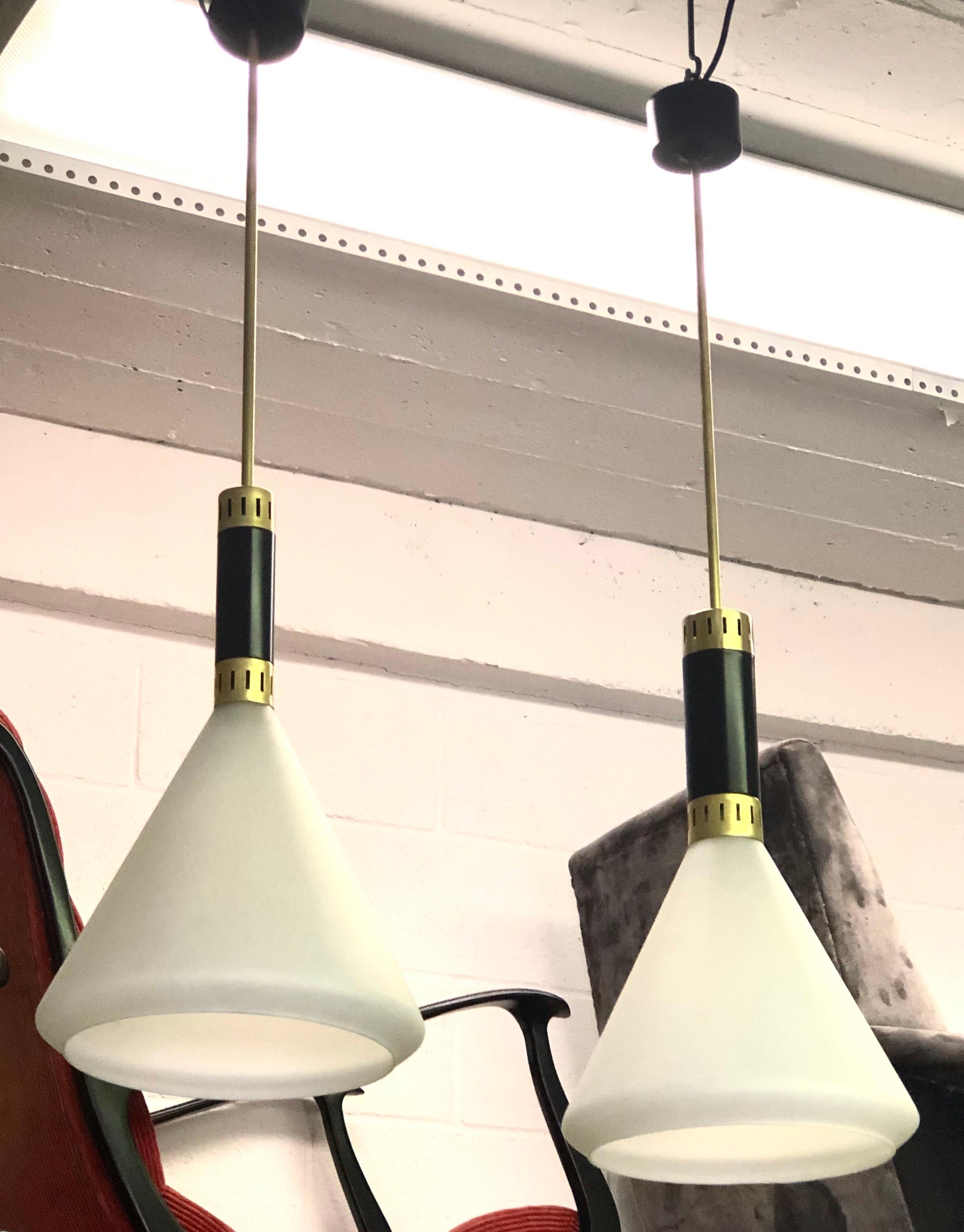 An Elegant Pair of Italian Mid-Century Modern pendants or chandeliers attributed Max Ingrand for Fontana Arte, circa 1958. The pieces are composed a black enameled metal and brass collar which supports a conical milk glass reflector which curves
