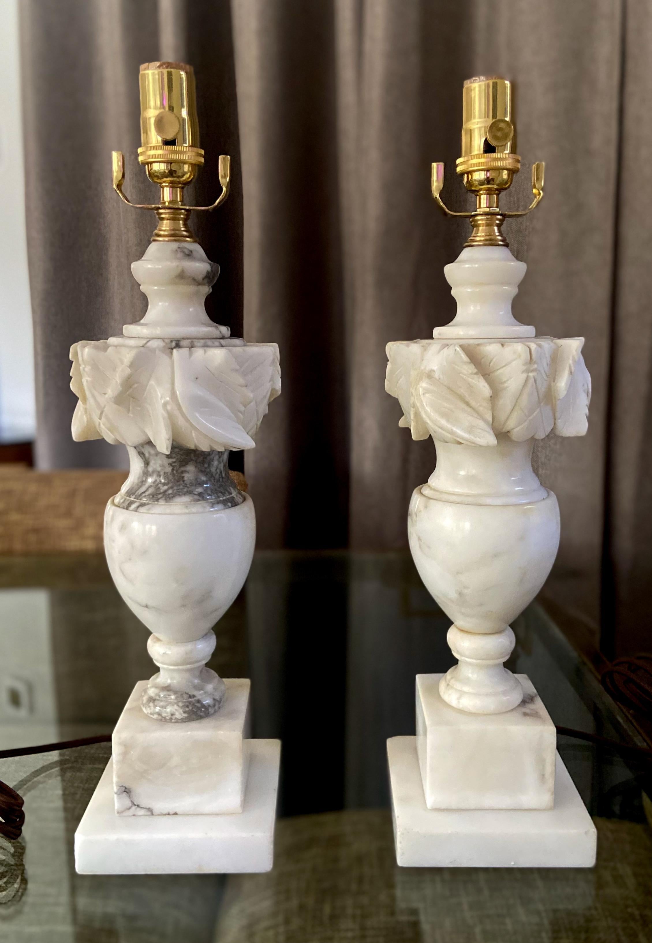 Pair of finely crafted hand carved neo-classic style urn form alabaster lamps. The intricately carved white alabaster are covered with lots natural colorful veining. Newly wired with 3 way sockets and rayon covered cords.

