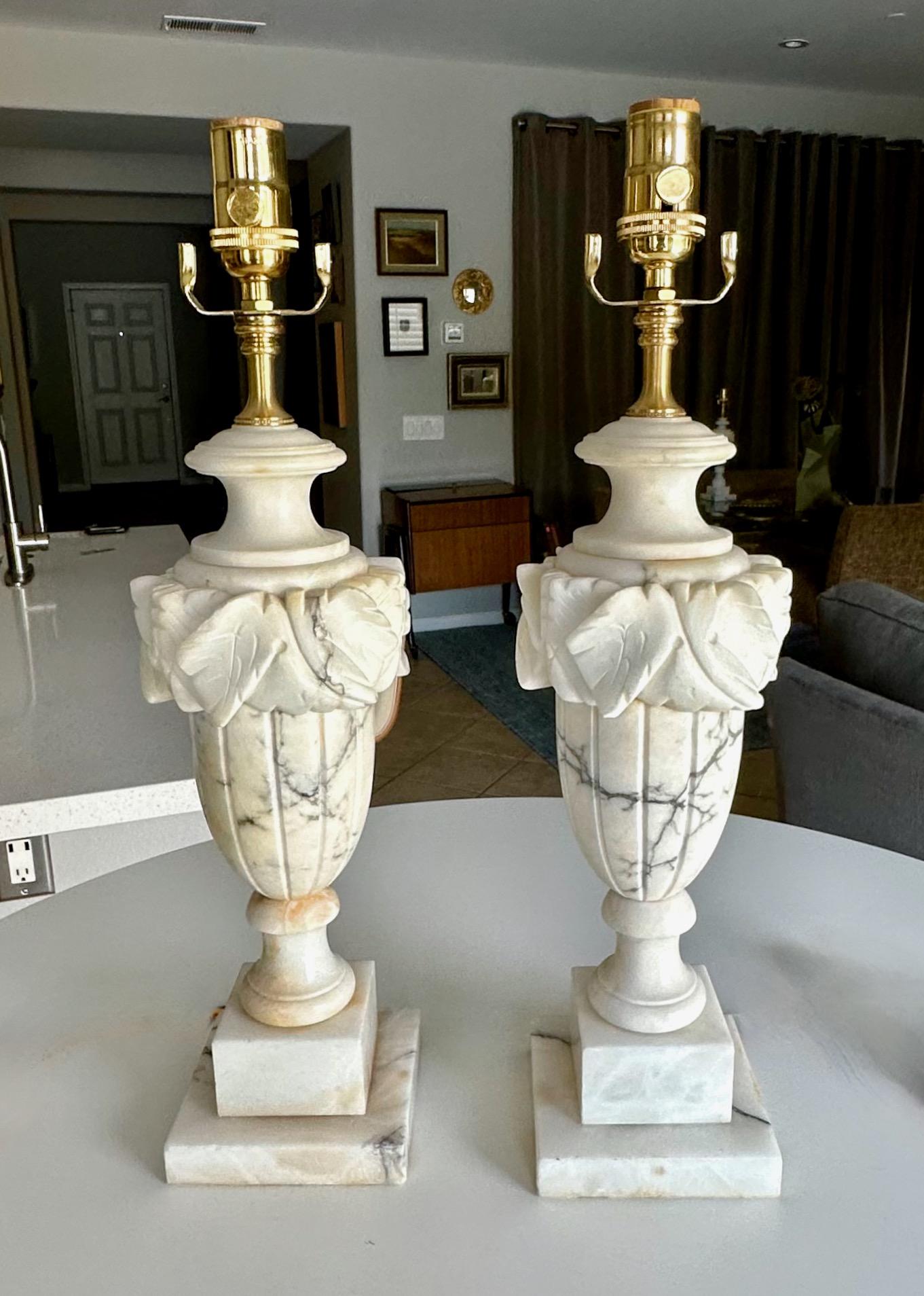 Paire de grandes lampes en albâtre de style néo-classique finement sculptées à la main en forme d'urne. Les albâtres blancs sculptés de manière complexe sont recouverts de nombreuses veines colorées naturelles.  Nouveau câblage avec prises de