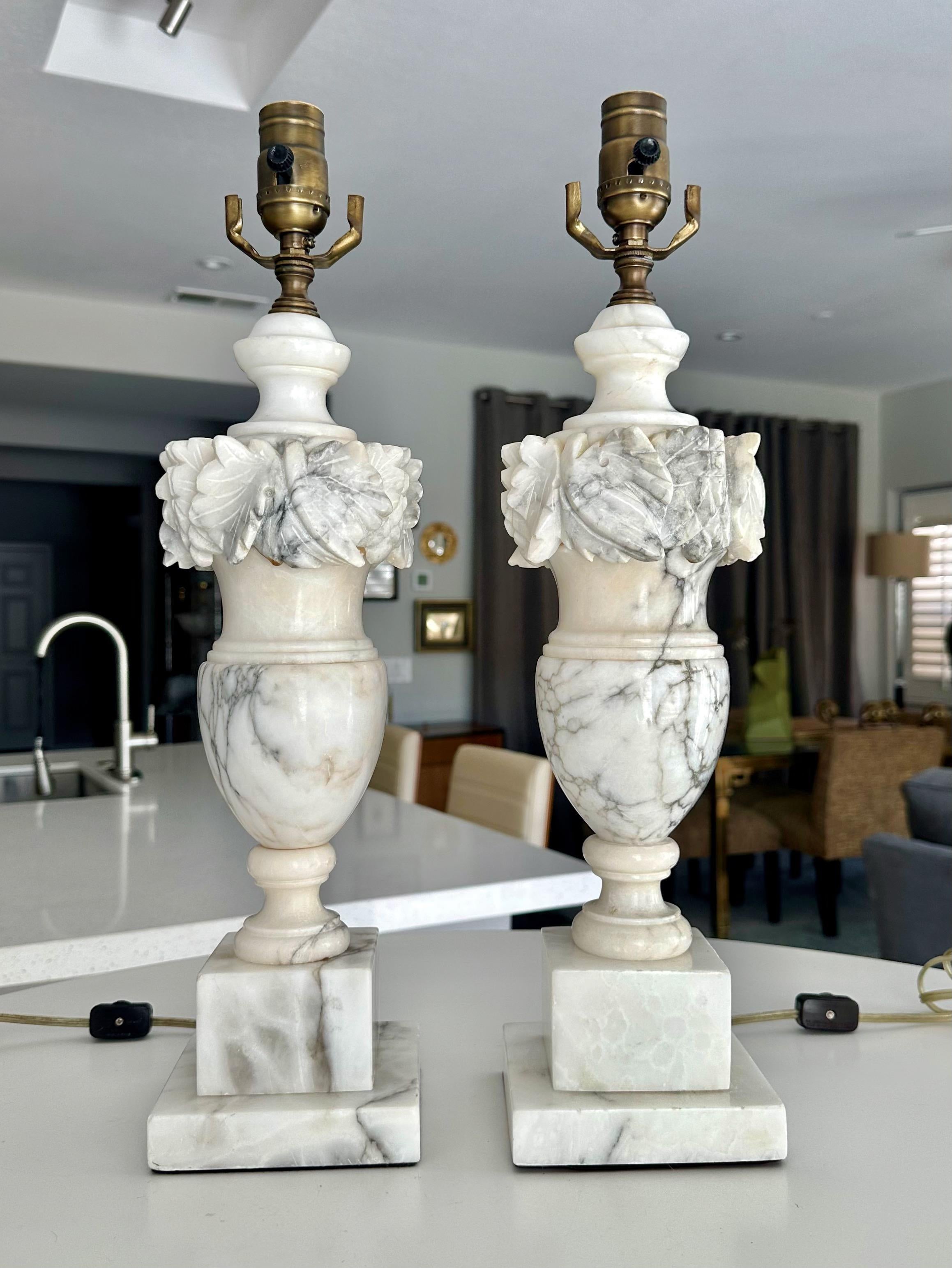 Pair of finely crafted hand carved neo-classic style urn form alabaster lamps. The intricately carved white alabaster are covered with lots natural colorful veining.  
Overall height top of socket 20