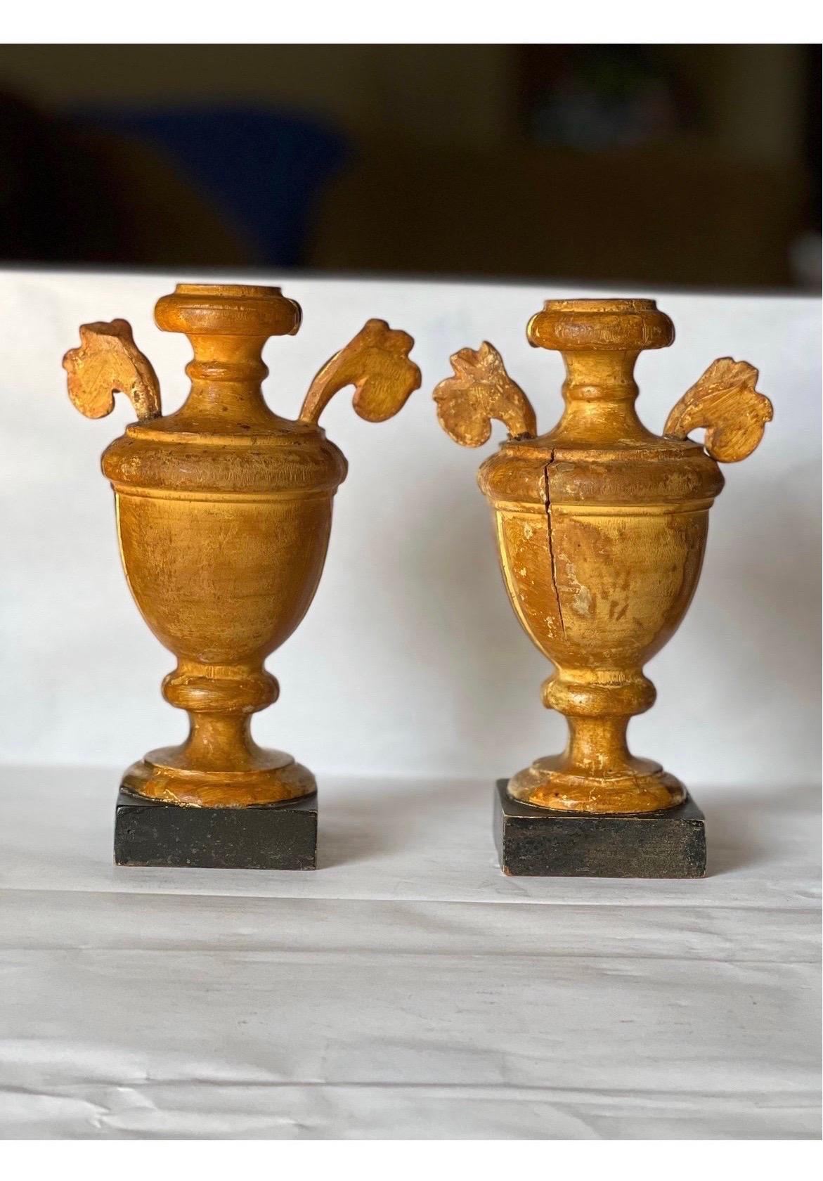 A beautiful pair of antique likely circa 1900 Italian Gilt wood ornamental urns with carved and fluted bodies, foliate handles which rest on faux marble bases. No marks. Tops with holes - as shown.