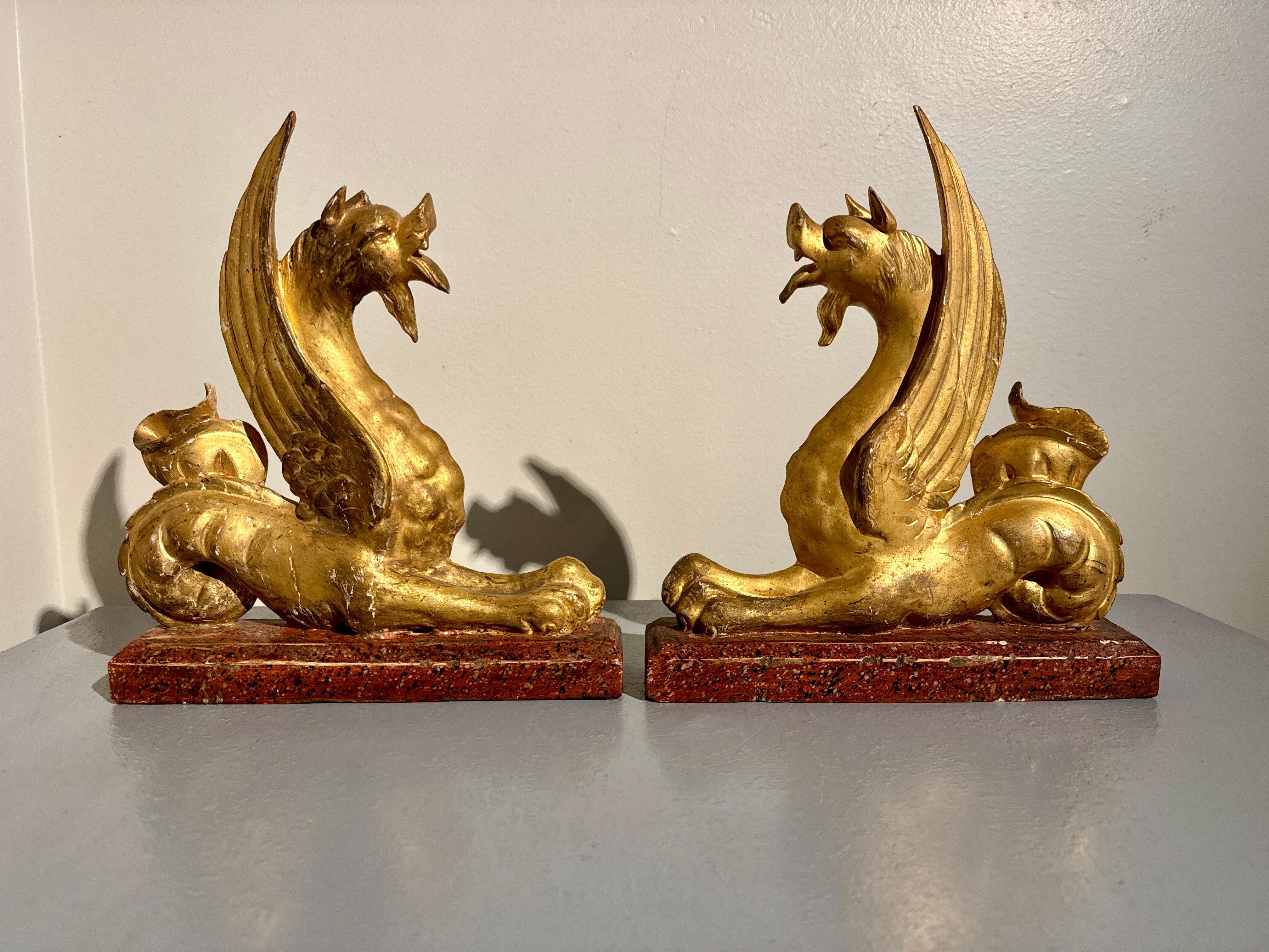 A powerful and dramatic pair of Italian neoclassical carved and gilt wood mythical animal figures on faux painted bases, mid 19th century or earlier, Italy.

The fantastic beasts are well carved, with dramatic wings that follow the sensuous curve of