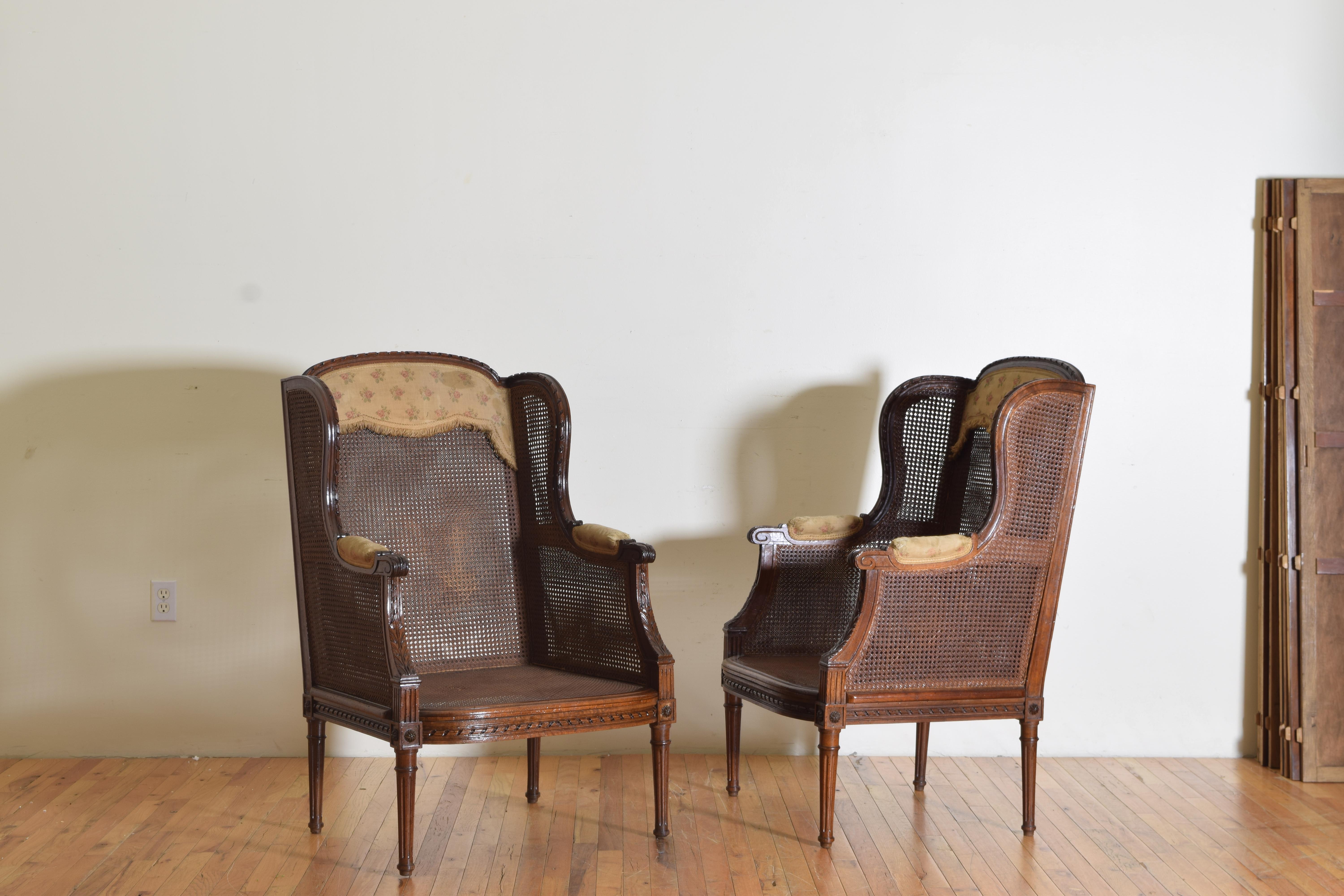 having rounded backrests and winged sides, completely upholstered in caning, with carved arms and carved round tapering legs, the backrests and armrests retaining original upholstery, lacking cushions.