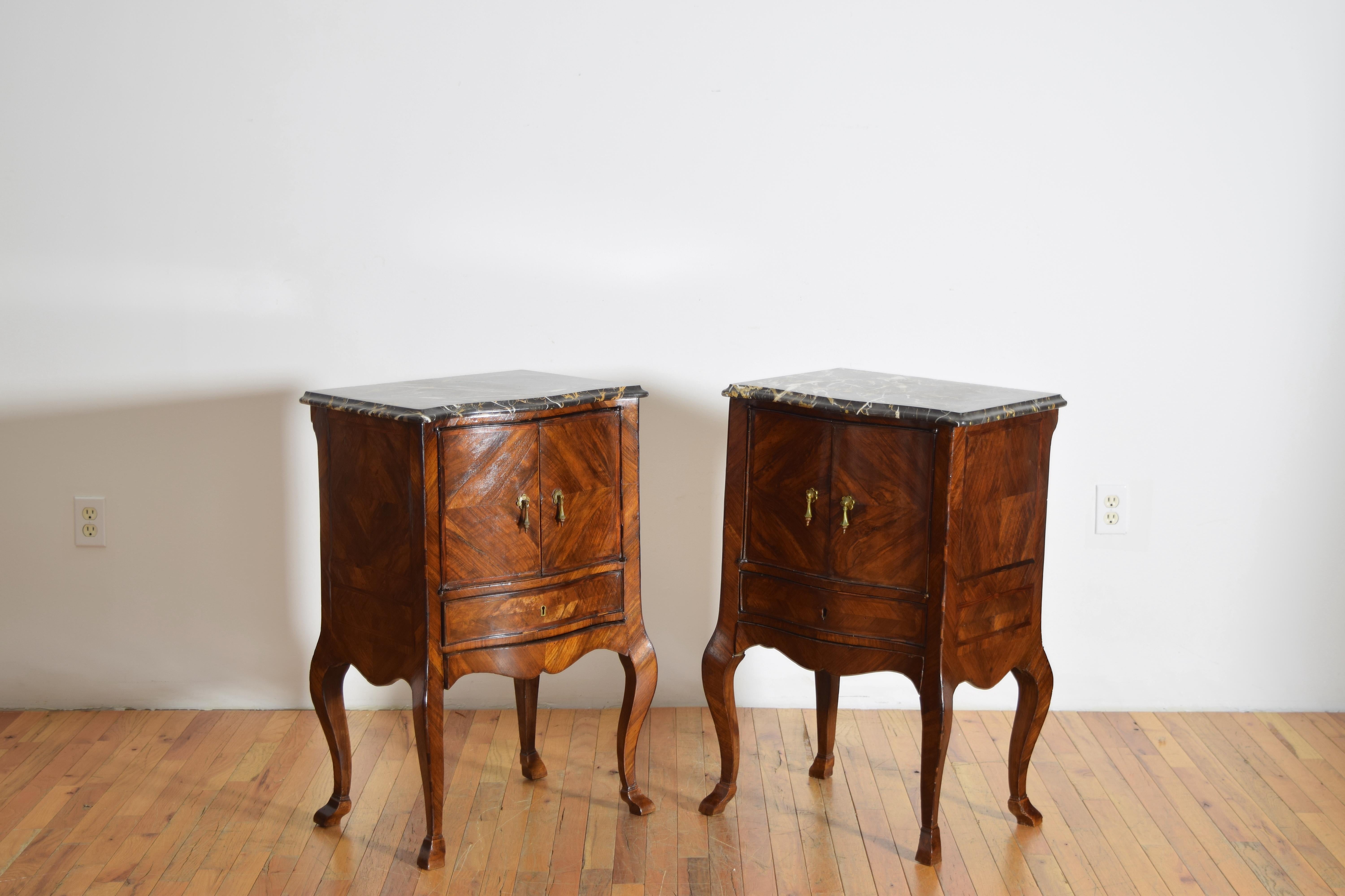 highly stylized these commodes feature Portoro marble tops with serpentine shaped fronts, the conforming cases richly veneered in beautifully grained walnut veneers with two doors atop two drawers (one hidden at bottom), raised on cabriole legs