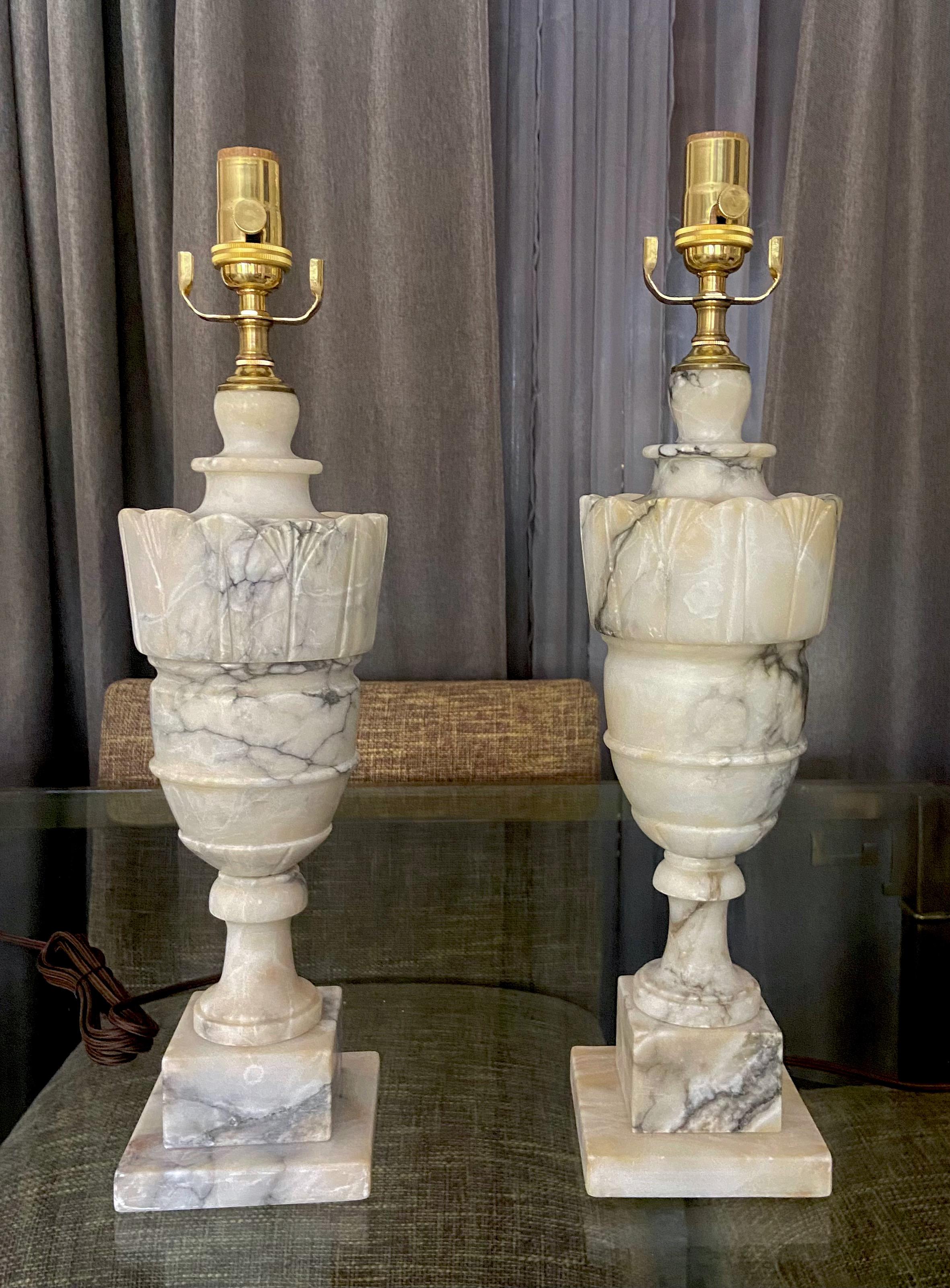 Pair of finely crafted hand carved neo-classic style urn form alabaster lamps. The intricately carved white alabaster (with highlights of tan) are covered with lots natural colorful veining. Newly wired with 3 way sockets and rayon covered
