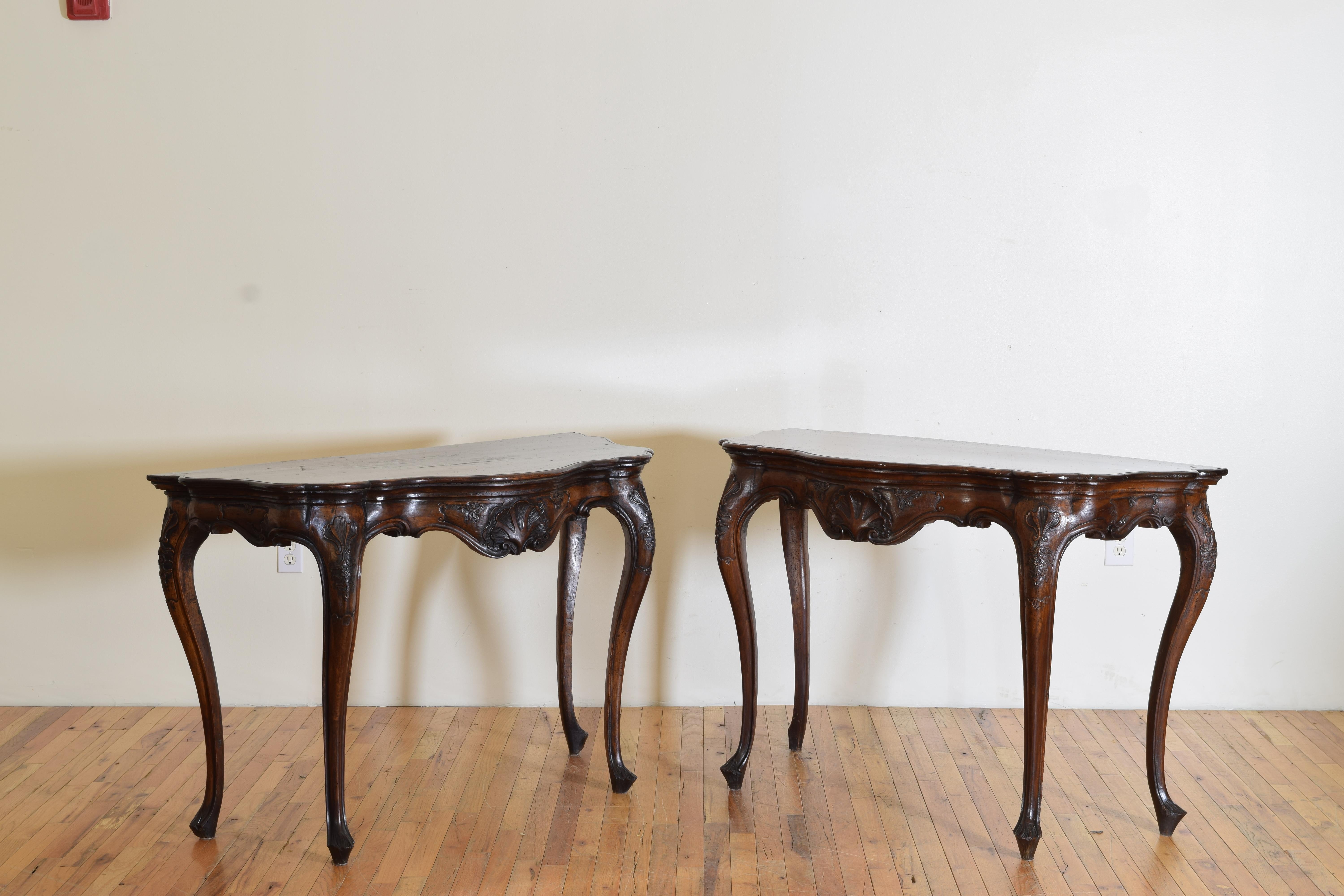 Each console having serpentine shaped tops with molded edges atop conforming frames with beautifully hand-carved motifs of shells and scrolls, raised on shaped and carved legs ending on raised feet