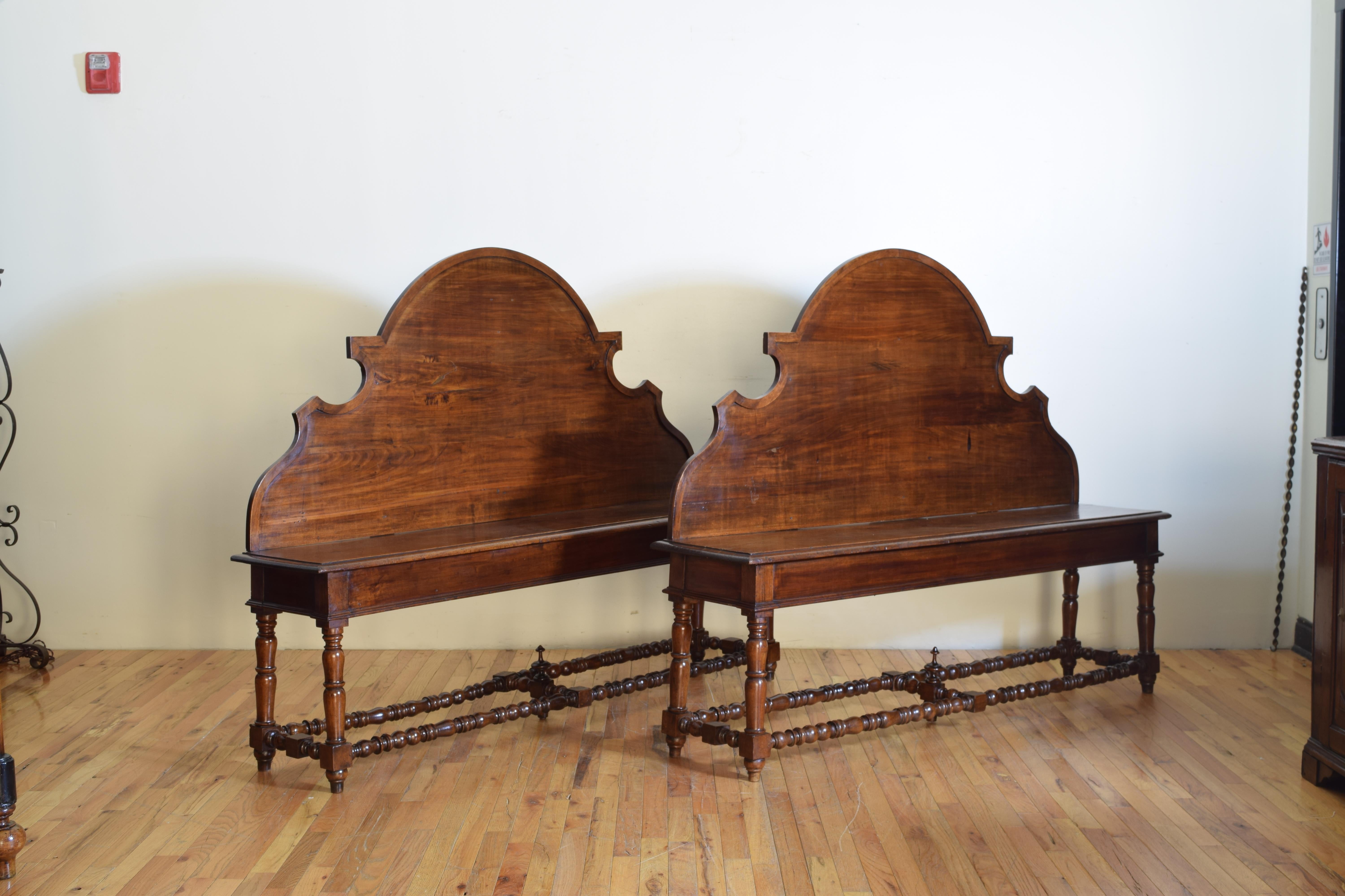 This well sized, as in manageable, pair of benches has Baroque shaped tall backrests above rectangular seats with molded edges, the underside of one of the seats with a secret storage area, raised on turned legs joined by turned box stretchers, the