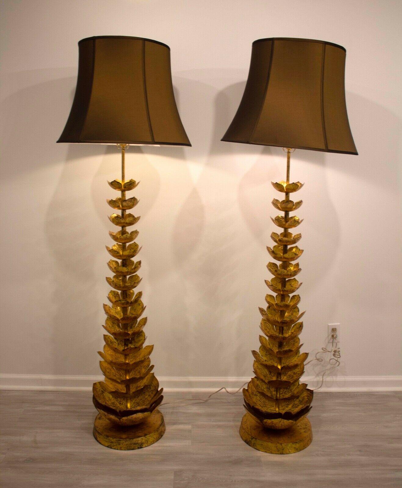 This monumental pair of Jamie Young floor lamps are a stunning pair for any room and feature gold gilt ascending blooming lotuses made of metal and finished in a rich, antique gold leaf. Both are topped with a warm gold and brown shade. In very good