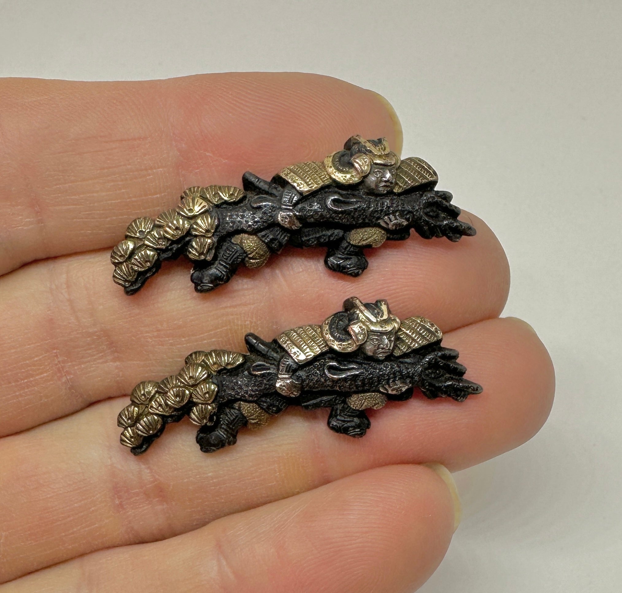 This is a very rare pair of Antique Victorian Shakudo Brooch Pins from Japan depicting a Samurai Warrior holding a Sea Dragon swimming through Lily Pads.  The extraordinary imagery is full of history, drama and mystique.  The dragons are wonderful,