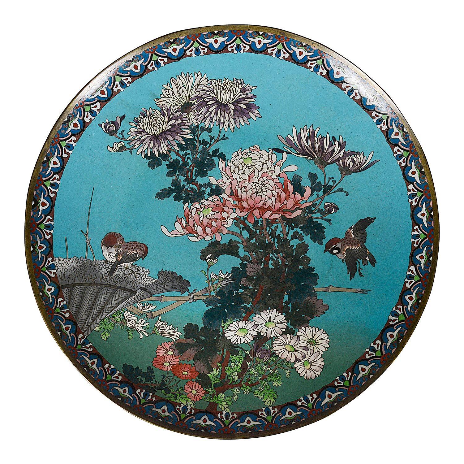 This exquisite pair of Japanese Meiji period cloisonné enamel chargers showcases the intricate artistry typical of the era. Each charger features a vibrant turquoise background, adorned with detailed depictions of chrysanthemums and other floral