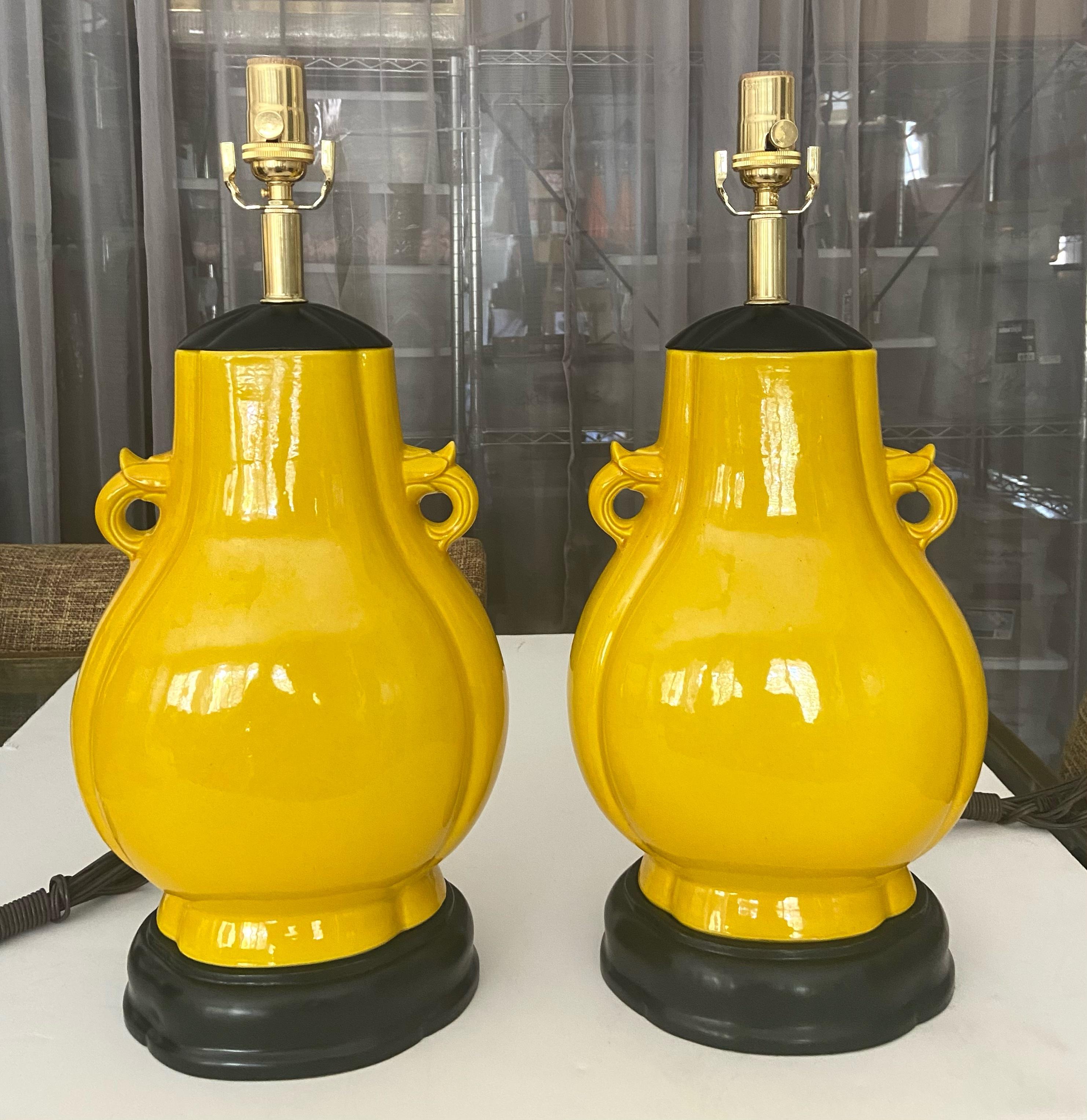 Paire de lampes de table en porcelaine japonaise de forme ovoïde aplatie, jaune et monochrome. Les vases jaune vif sont flanqués de poignées, montés sur leur base et leur couvercle en bois tourné sculpté et laqué noir d'origine. Le câblage a été