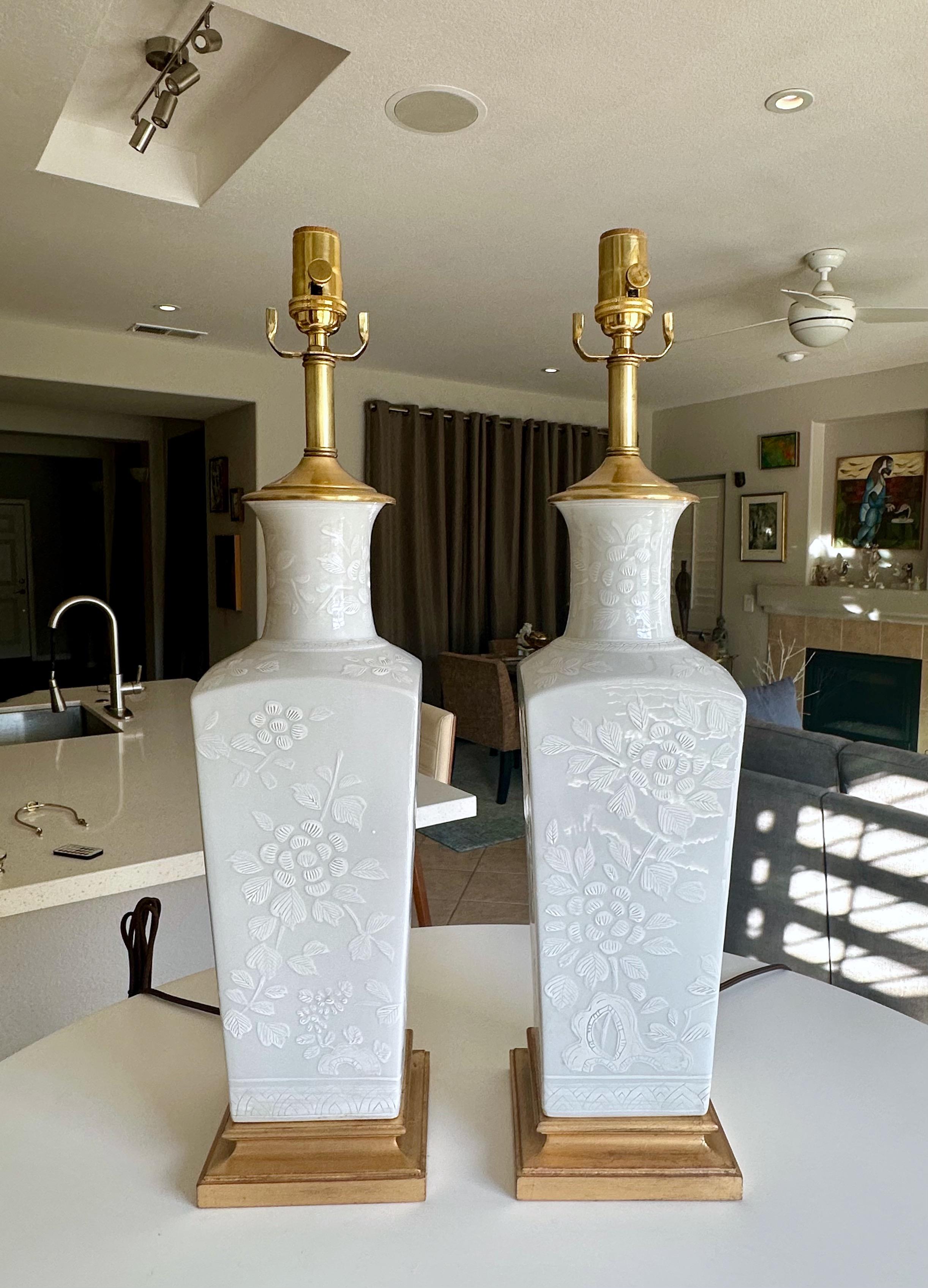 Pareja de lámparas de sobremesa japonesas asiáticas blanc de shine monocromas de porcelana en forma de jarrón cuadrado. Montadas sobre bases de madera dorada torneada. Los jarrones están decorados con motivos florales en relieve. Recién cableada con