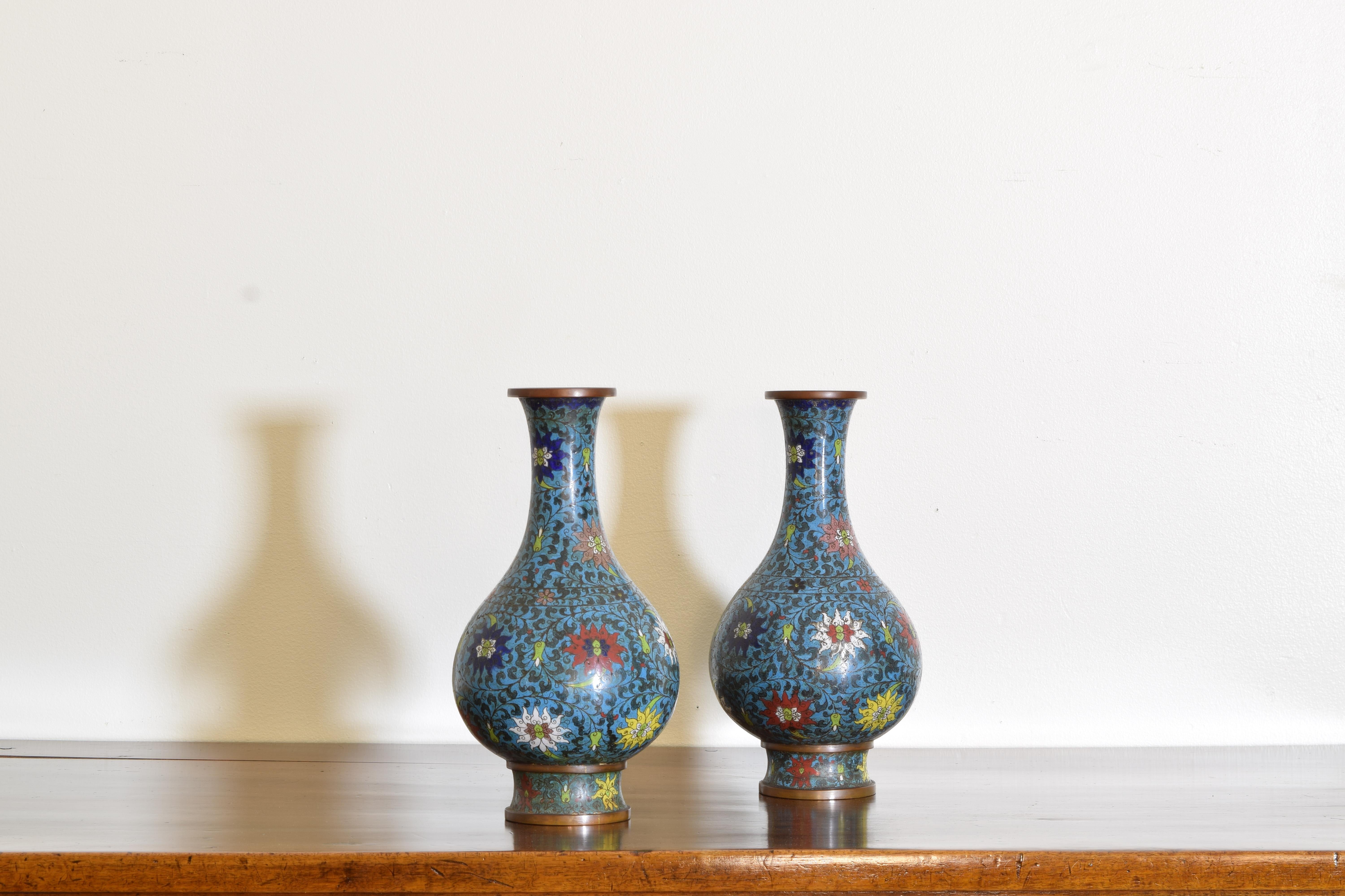 Brass vases with a turquoise leaf field background with a bright floral ground, flowers of white, red, and cobalt blue, the bottoms decorated with leaves and a single flower