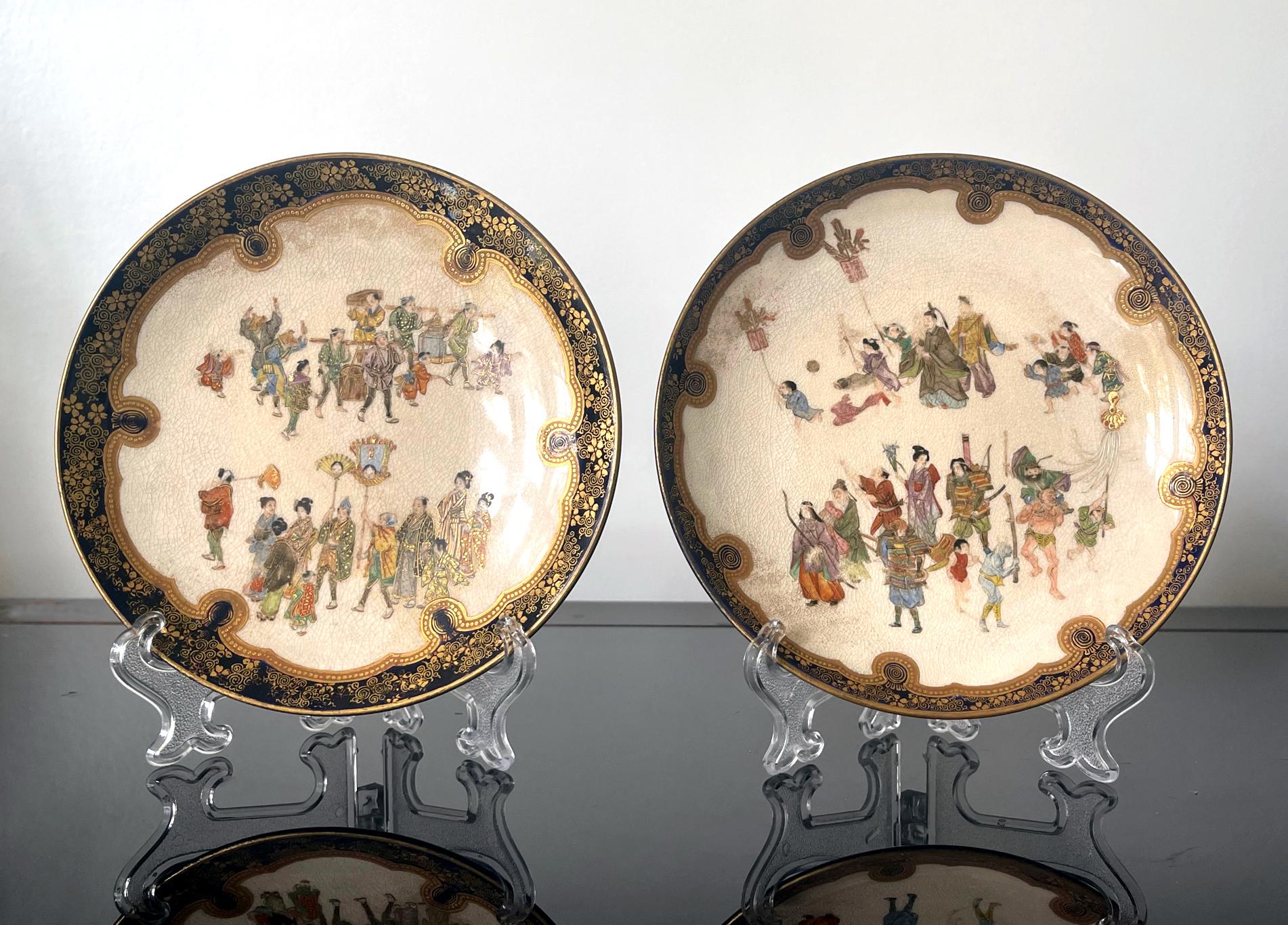 A pair of Satsuma ceramic plates made by Kinkozan studio circa 1880-1900s during the late Meiji Period. Each dish features miniature enamel decoration of two lively festival scenes within a cobalt blue border laced with gold scrolls ornamentation.
