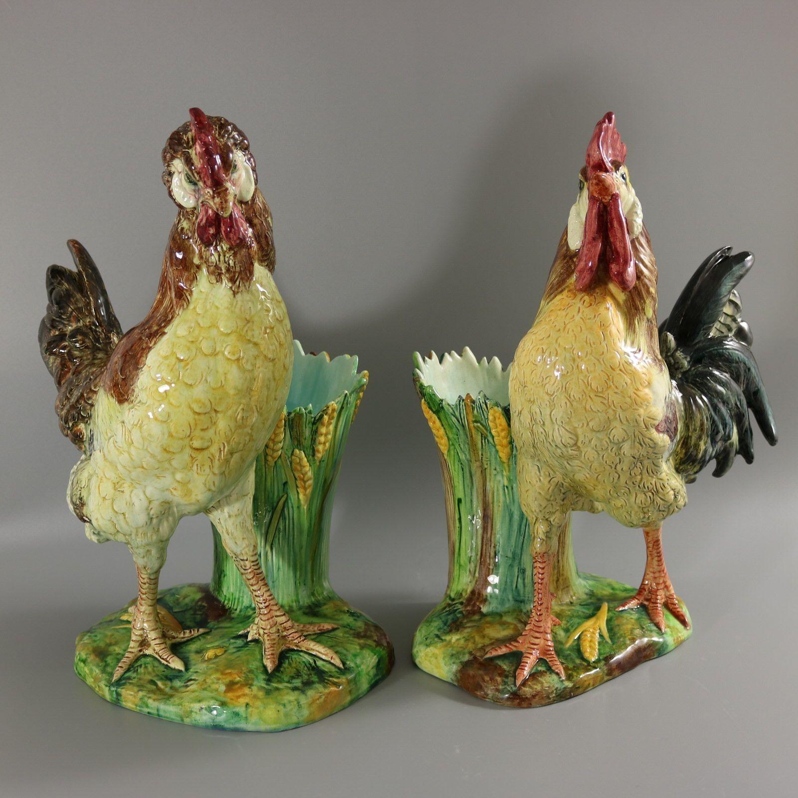 Pair of Jerome Massier Fils Majolica figural vases which feature a hen and a rooster, stood in front of a vase. The vase has leaves and wheat around the sides. Colouration: brown, yellow, green, are predominant. The rooster bears maker's marks for