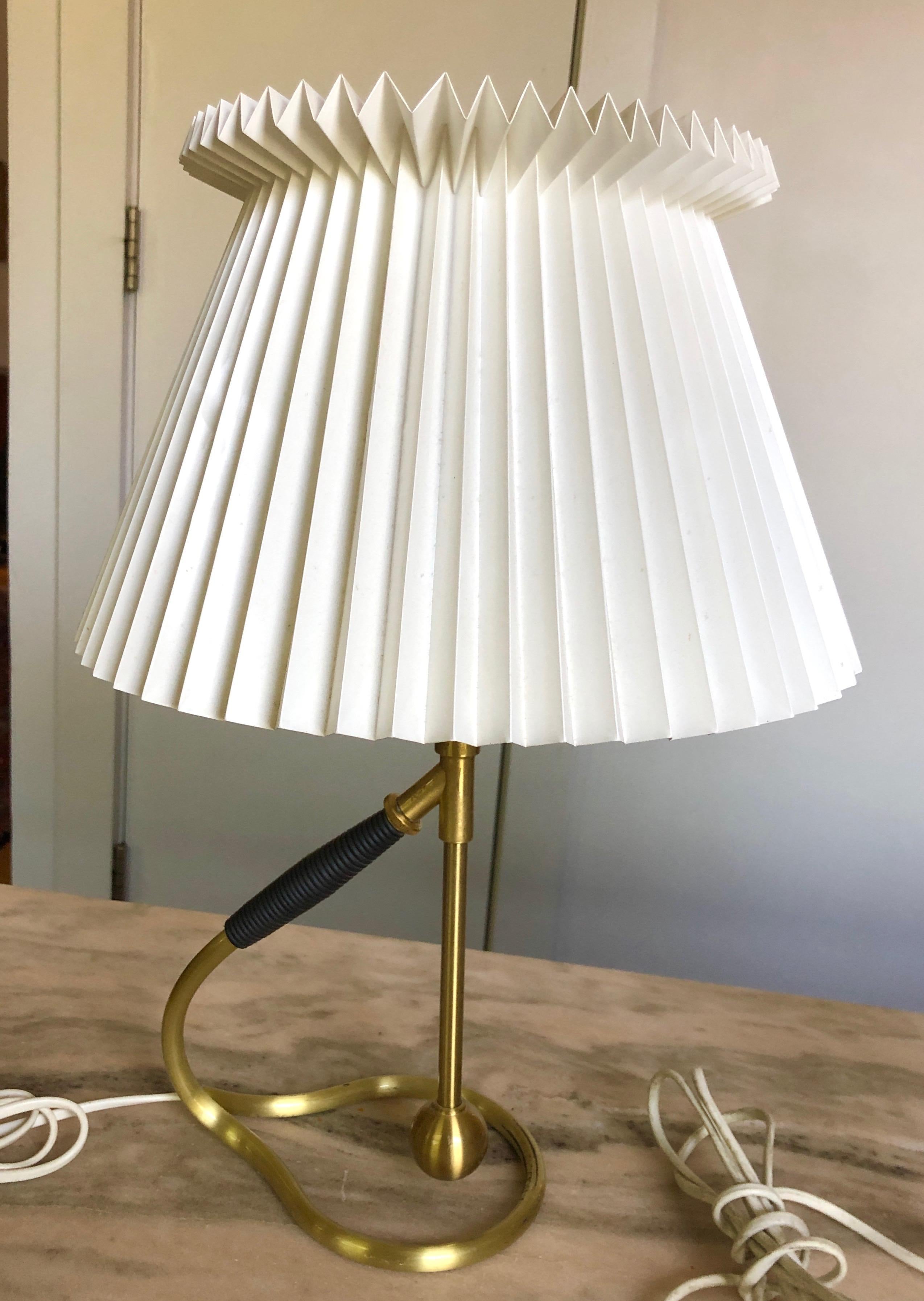 Brushed brass, faux leather wrapped handle, original pleated shade. Designed in the 1940s, this vintage pair is likely from the 1960s. The sculptural ingeniously transforms from table lamp to wall sconce by tilting the free-floating pendulum in the