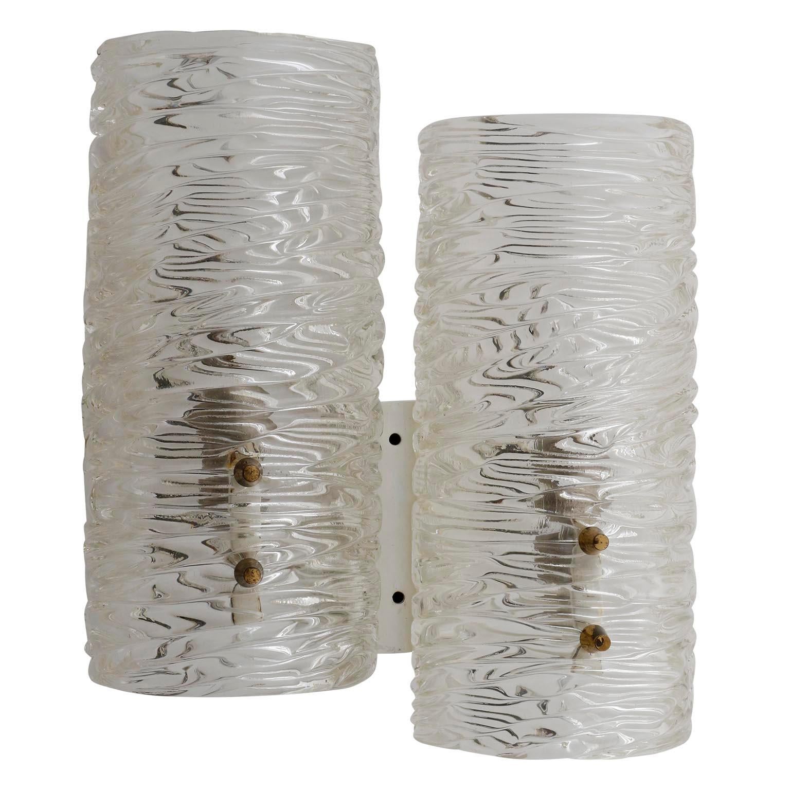 A pair of textured glass wall lamps by J.T. Kalmar, Austria, manufactured in midcentury, circa 1960 (late 1950s or early 1960s).
Two half round curved glasses are mounted with cone shaped brass bolts on a white enameled backplate.
Each sconce has
