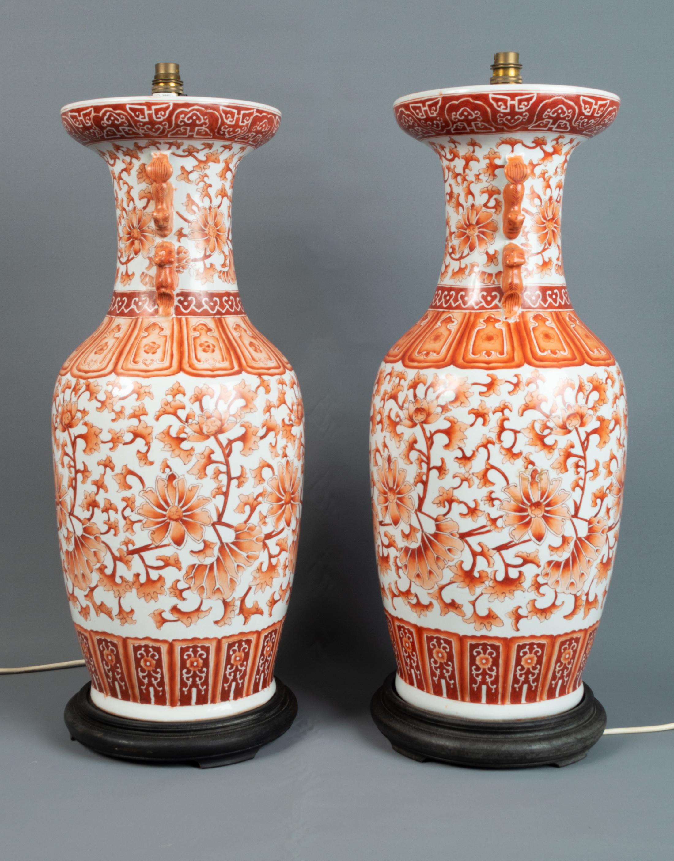 A pair of large 19th century Chinese porcelain lamp vases. 
China, C.1850

The white ground porcelain decorated in orange and rust foliate and flower motifs with foo dog applied handles. Mounted on wooden bases.

Free from chips, cracks or