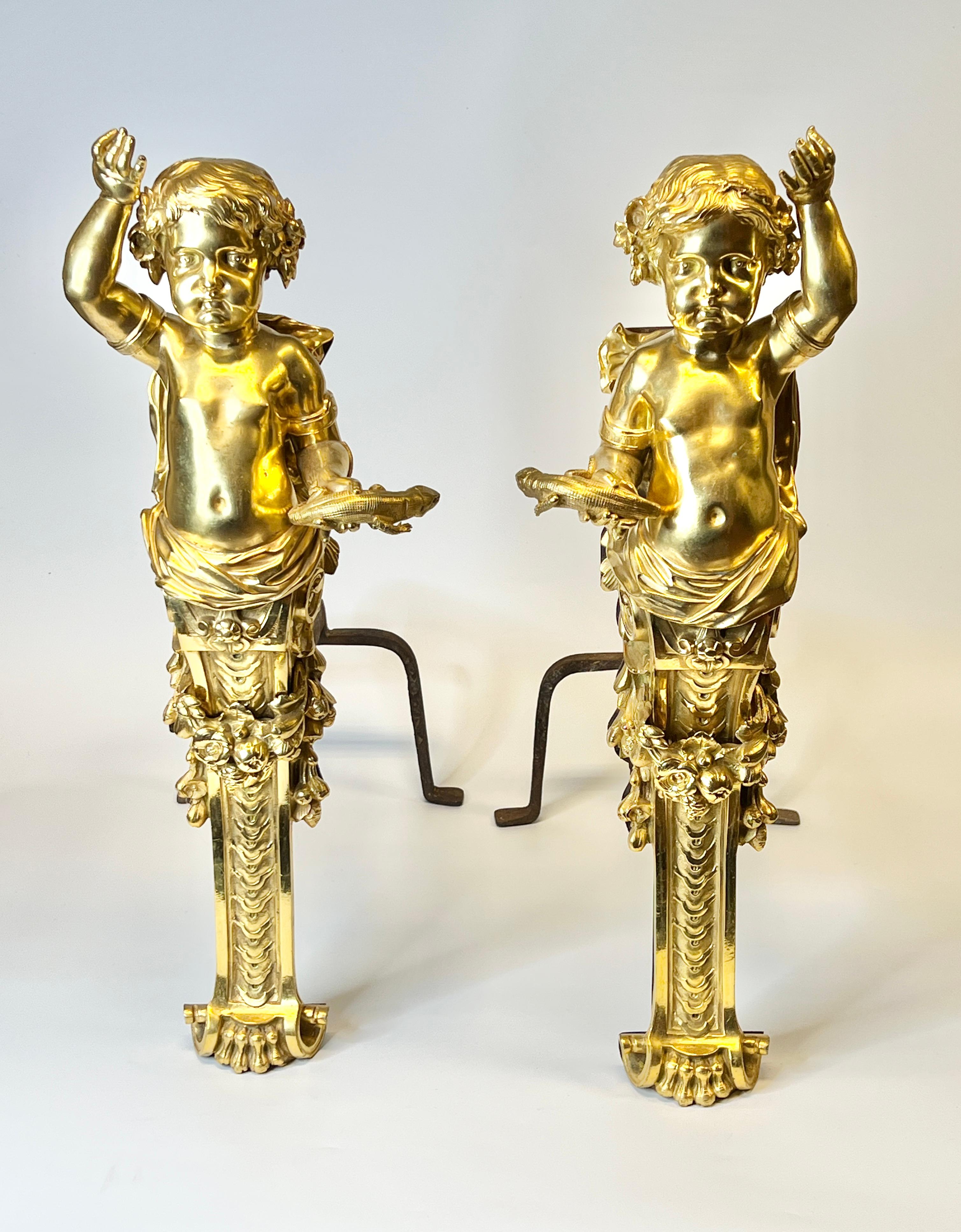Zwei antike (19. Jh.), fein geschnitzte und gegossene Bronze-Andirons (Chenets) im neoklassizistischen Stil mit vergoldeter Bronzepatina, die Putten darstellen.  Jeweils 26 1/2 Zoll hoch, 11 Zoll breit und 24 Zoll tief.  Offensichtlich unsigniert. 