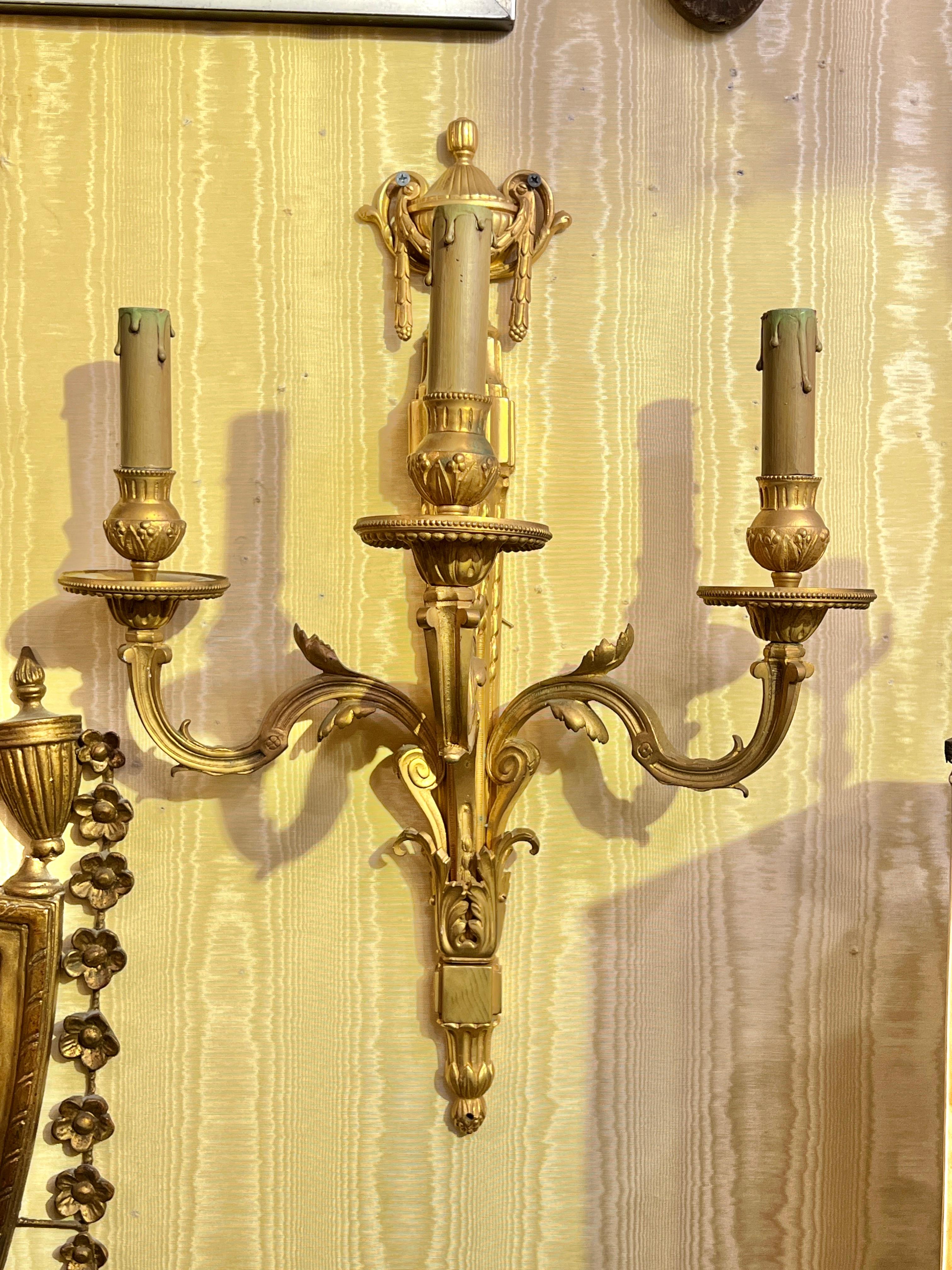 Pair of antique (19th century) gilt bronze three-light sconces in the French Louis XVI style, electrified with candelabra-size sockets, wiring and old faux-wax candle covers.  Each 23 1/2 by 17 1/4 by 9 1/2 inches.