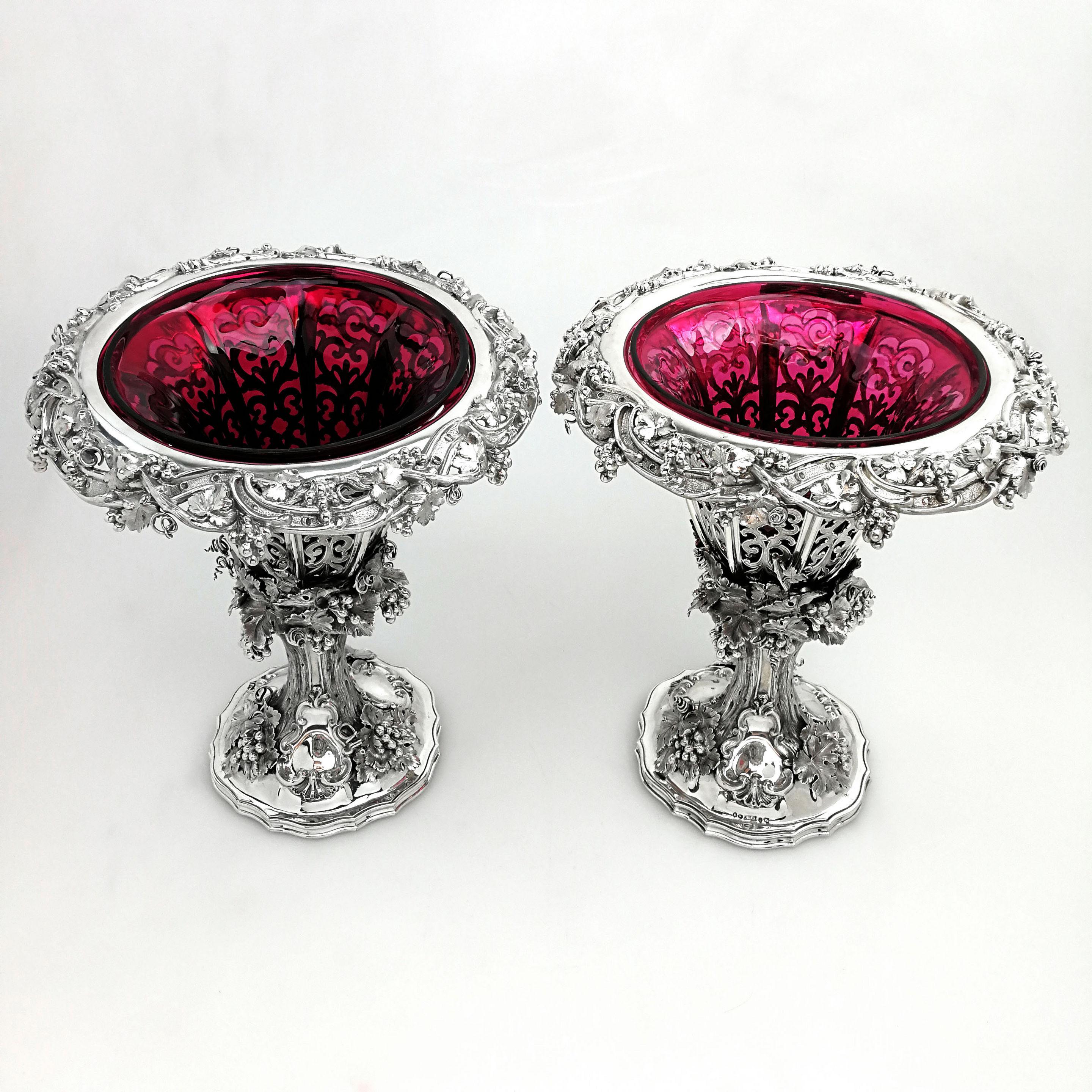 A pair of magnificent Victorian solid Silver Vases with claret coloured glass liners. The Vases have pierced panelled sides allowing the deep red liner to be visible and the body and foot of each Vase are decorated with ornate applied bunches of