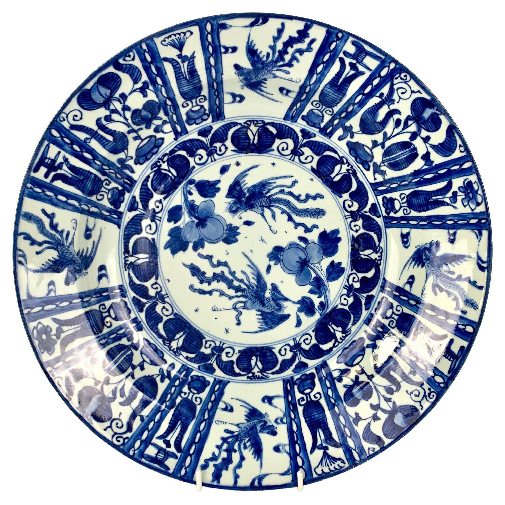 This pair of extraordinary chargers is hand-painted in a combination of beautifully soft and dark cobalt blue.
In the center, we see a pair of splendid phoenixes, a male and a female, chasing each other across the sky.
The male flies above with his
