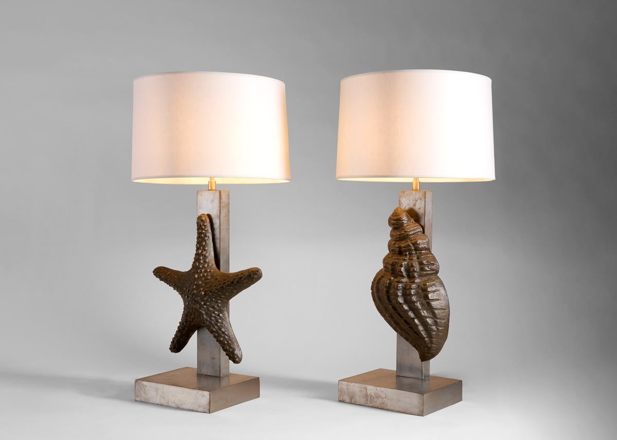 Une grande coquille de conque orne l'une de cette paire de lampes de table à motif marin, tandis que l'autre est ornée d'une étoile de mer. Chaque spécimen est rendu en bronze sombre et patiné, contrastant magnifiquement avec la base en acier et le