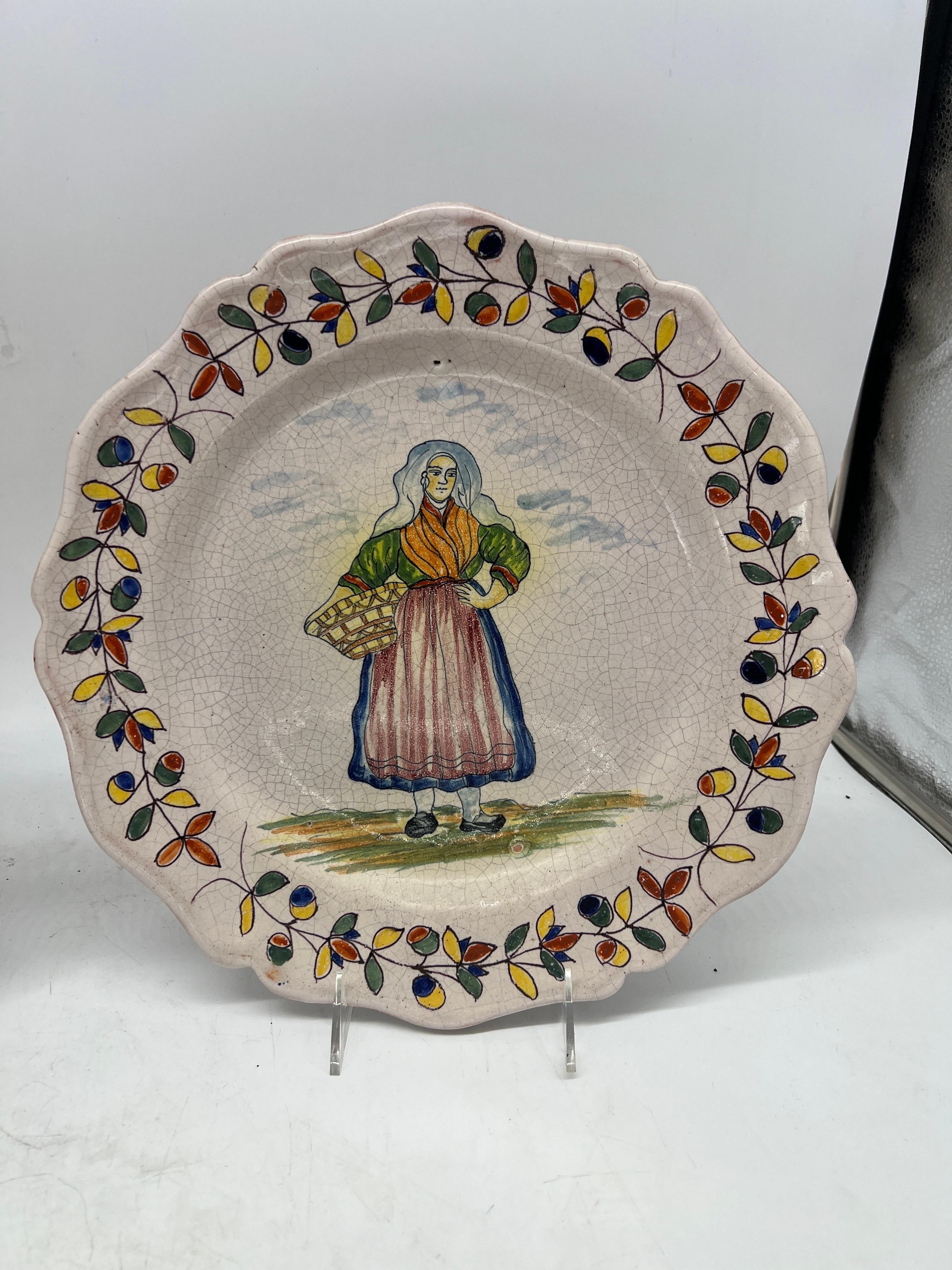 Quimper Pottery, French 20th century.

A pair of vintage Quimper faience pottery plates. Each plate has a hand painted and tin glazed figural surface and accented by a polychrome foliate leaf border. Marked to verso.