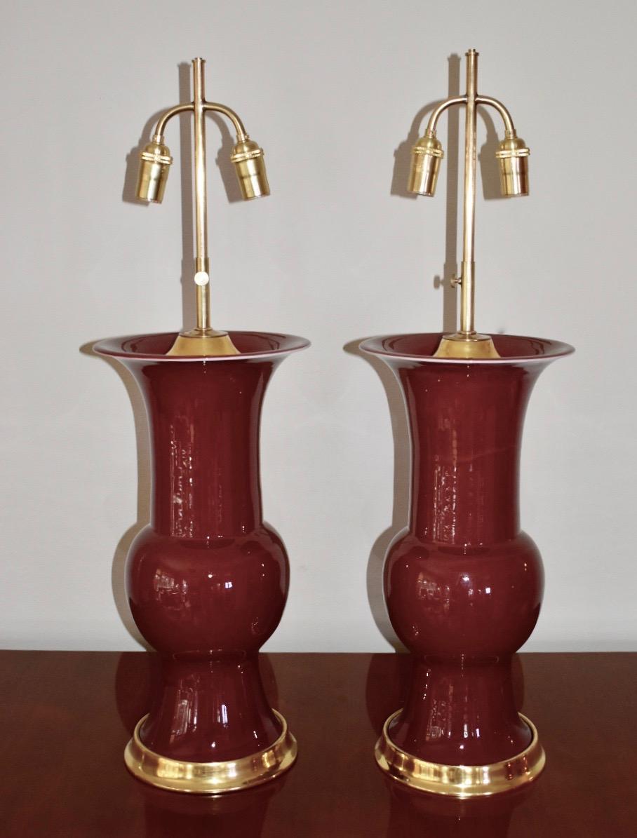 Large pair of sang de boeuf or oxblood red Chinese export vases converted to lamps on 23K water gilt turned wood lamp bases. Interior vase cap is also turned wood in a 23K water gilt finish. Newly wired for US with original French double cluster